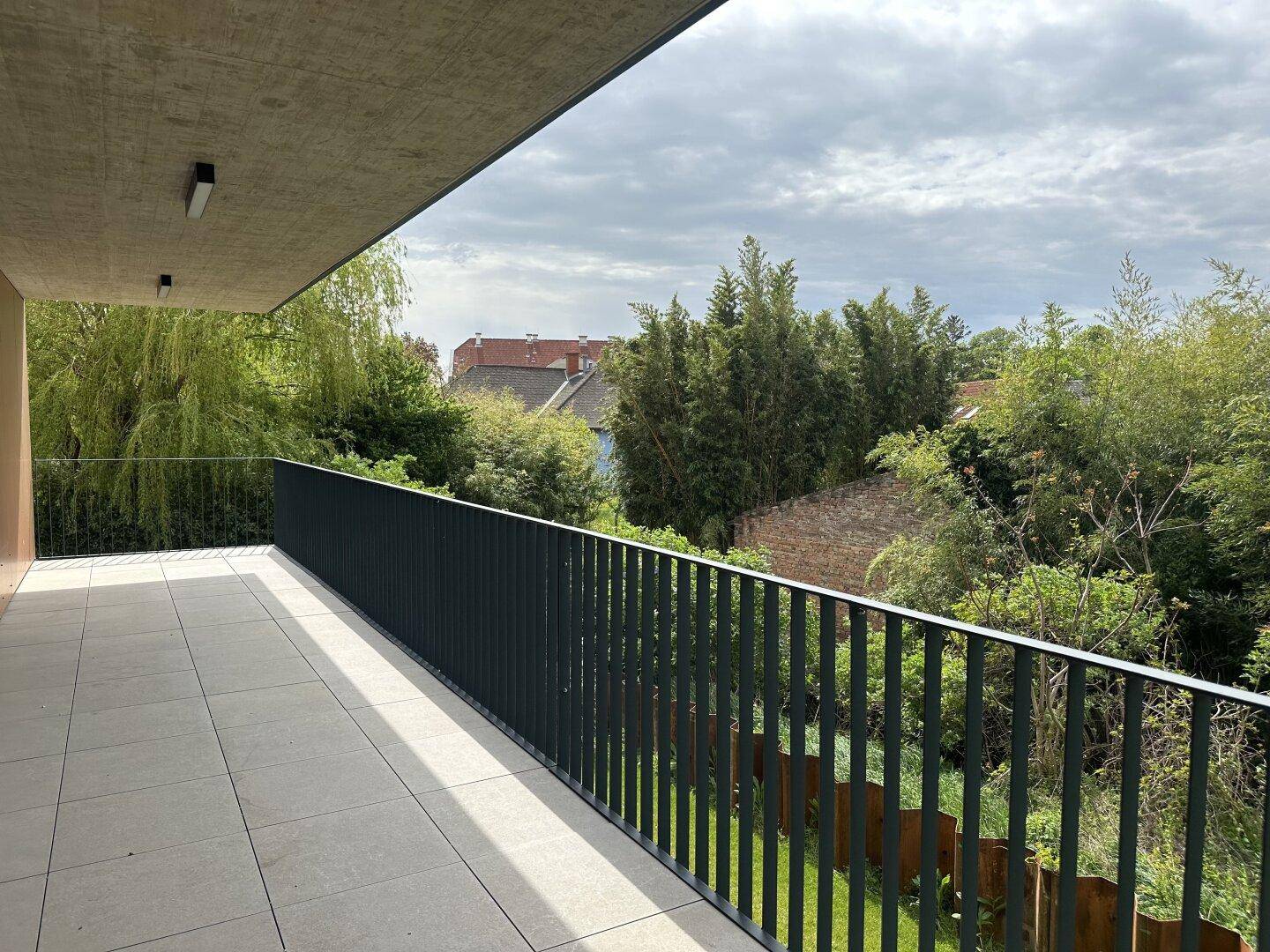 Großer Balkon mit Fliesenboden und weitem Blick ins Grüne, umgeben von Bäumen.