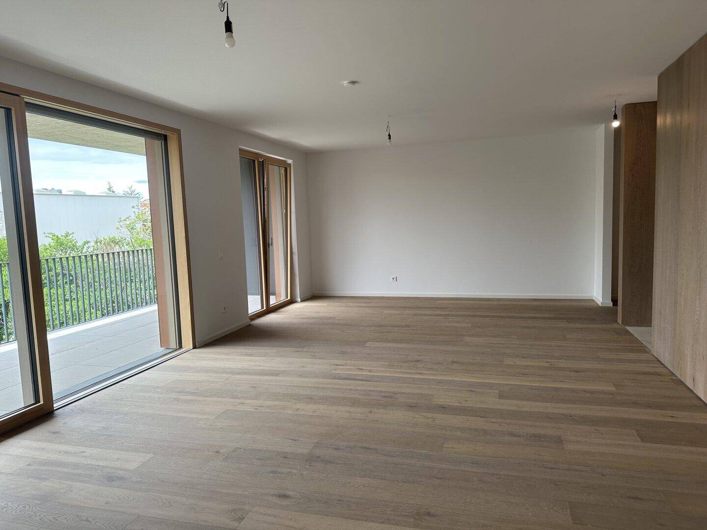 Heller, leerer Raum mit hochwertigem Holzplankenboden und großen Schiebetüren zum Balkon.