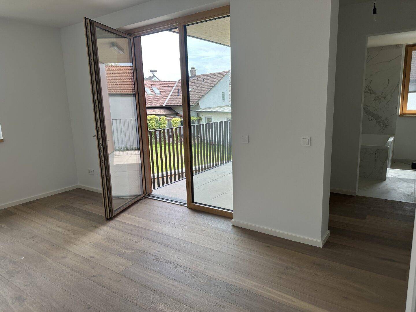 Helles Schlafzimmer mit Holzplankenboden und Zugang zum Balkon, angrenzend an ein modernes Bad.