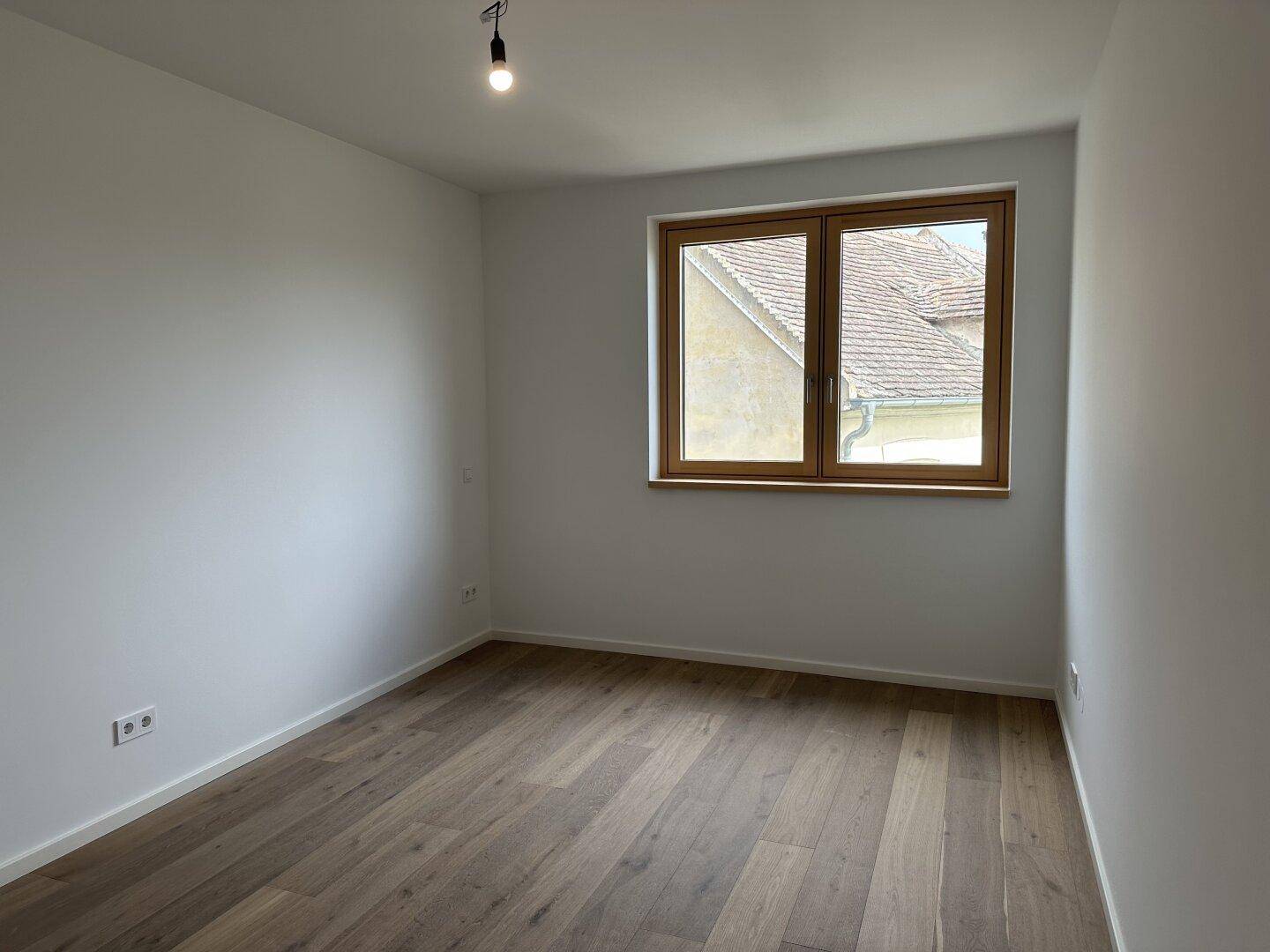 Ruhiges Schlafzimmer mit Holzplankenboden und einem Fenster mit Blick auf die Nachbarschaft.