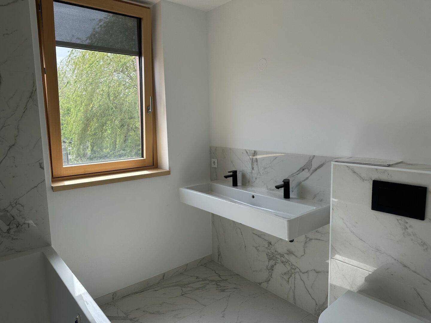 Modernes Badezimmer mit Marmorfliesen, Doppelwaschbecken, Badewanne und Fenster.