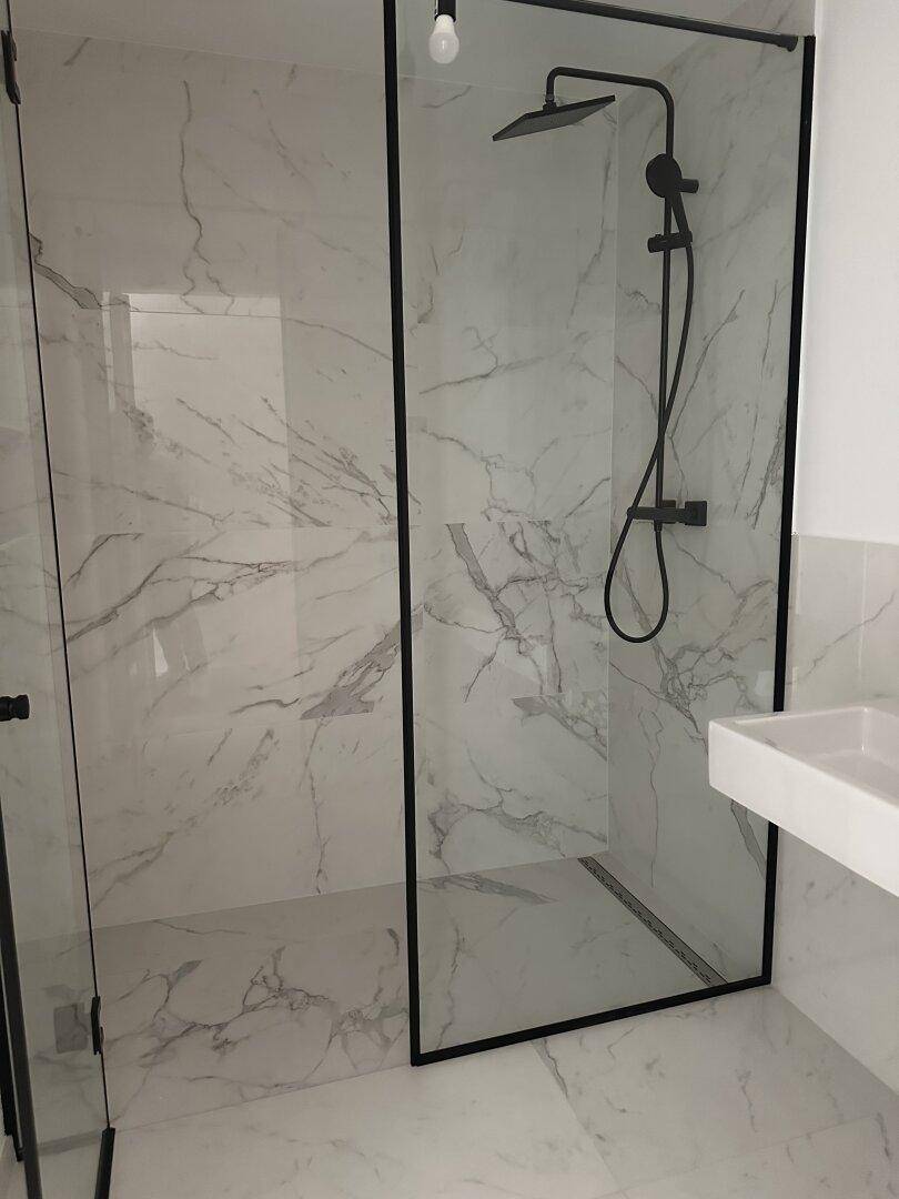 Elegantes Badezimmer mit Marmorfliesen, einer modernen begehbaren Dusche und schwarzer Armatur.