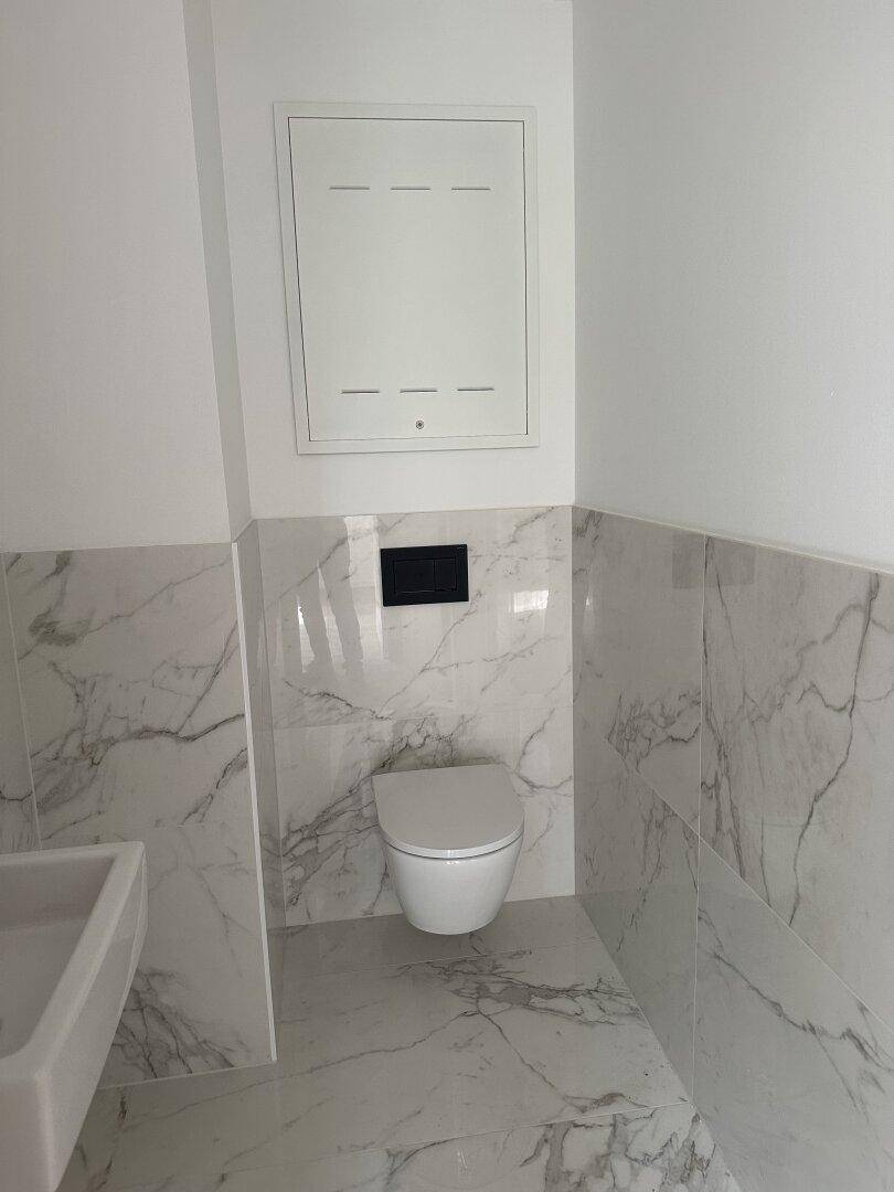 Modernes Gäste-WC mit Marmorfliesen, wandhängender Toilette und elegantem Waschbecken.