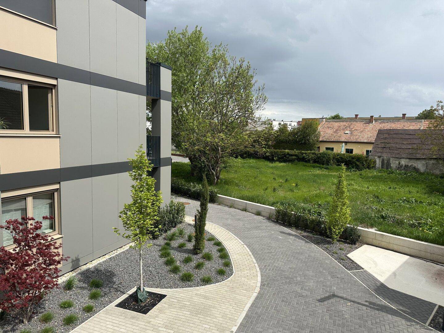Außenbereich mit gepflastertem Weg, begrünten Beeten und der modernen Fassade des Gebäudes.