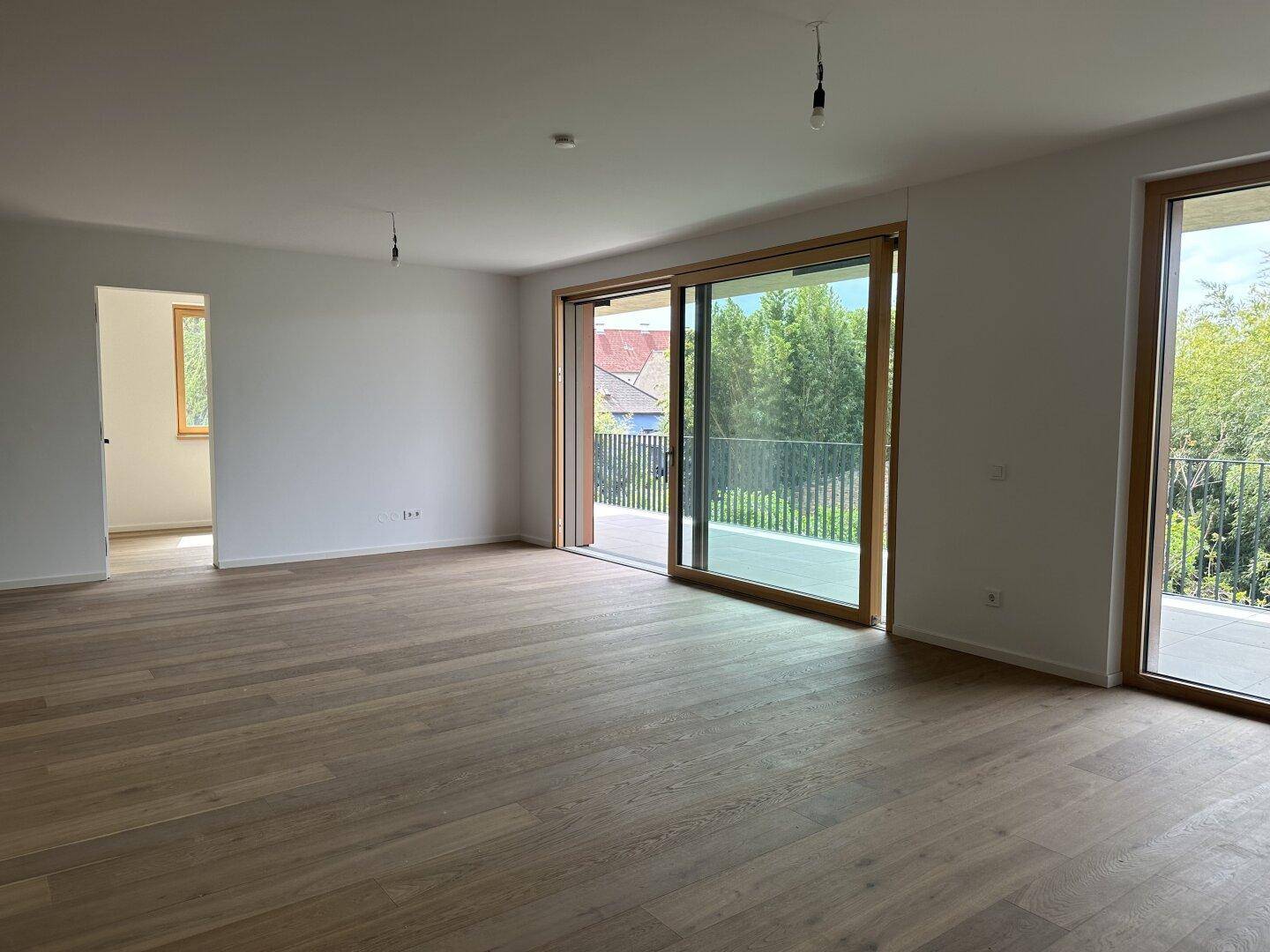 Heller Wohnraum mit Holzplankenboden und großen Fenstern, die Zugang zum Balkon bieten.