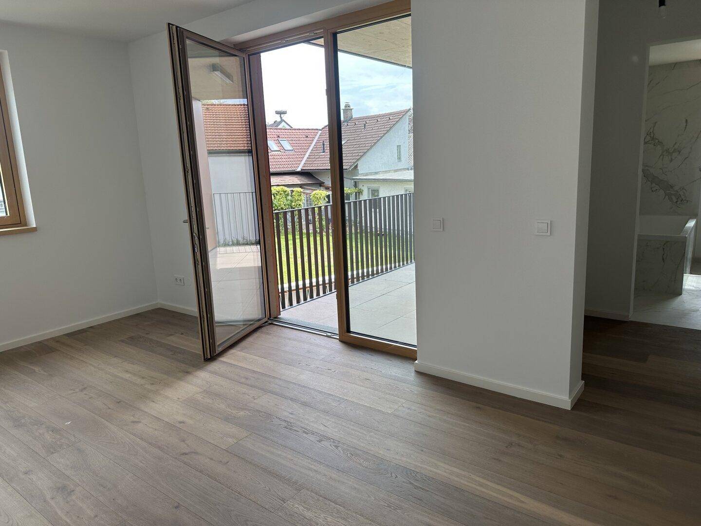 Schlafzimmer mit Holzplankenboden und direktem Zugang zu einem sonnigen Balkon.