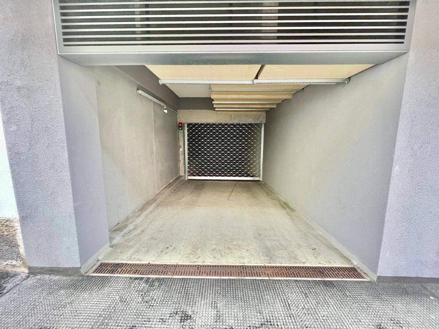 Einfahrt zur Tiefgarage mit Rolltor und Entwässerungsrinne im Außenbereich.