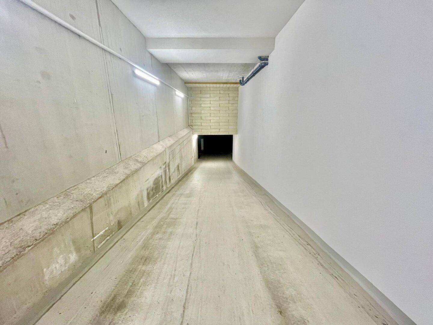 Lange Betonrampe führt in die unterirdische Parkgarage mit heller Beleuchtung.