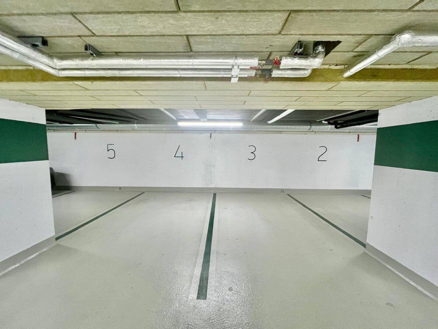 Leerer Bereich einer Tiefgarage mit nummerierten Stellplätzen und Deckenbeleuchtung.