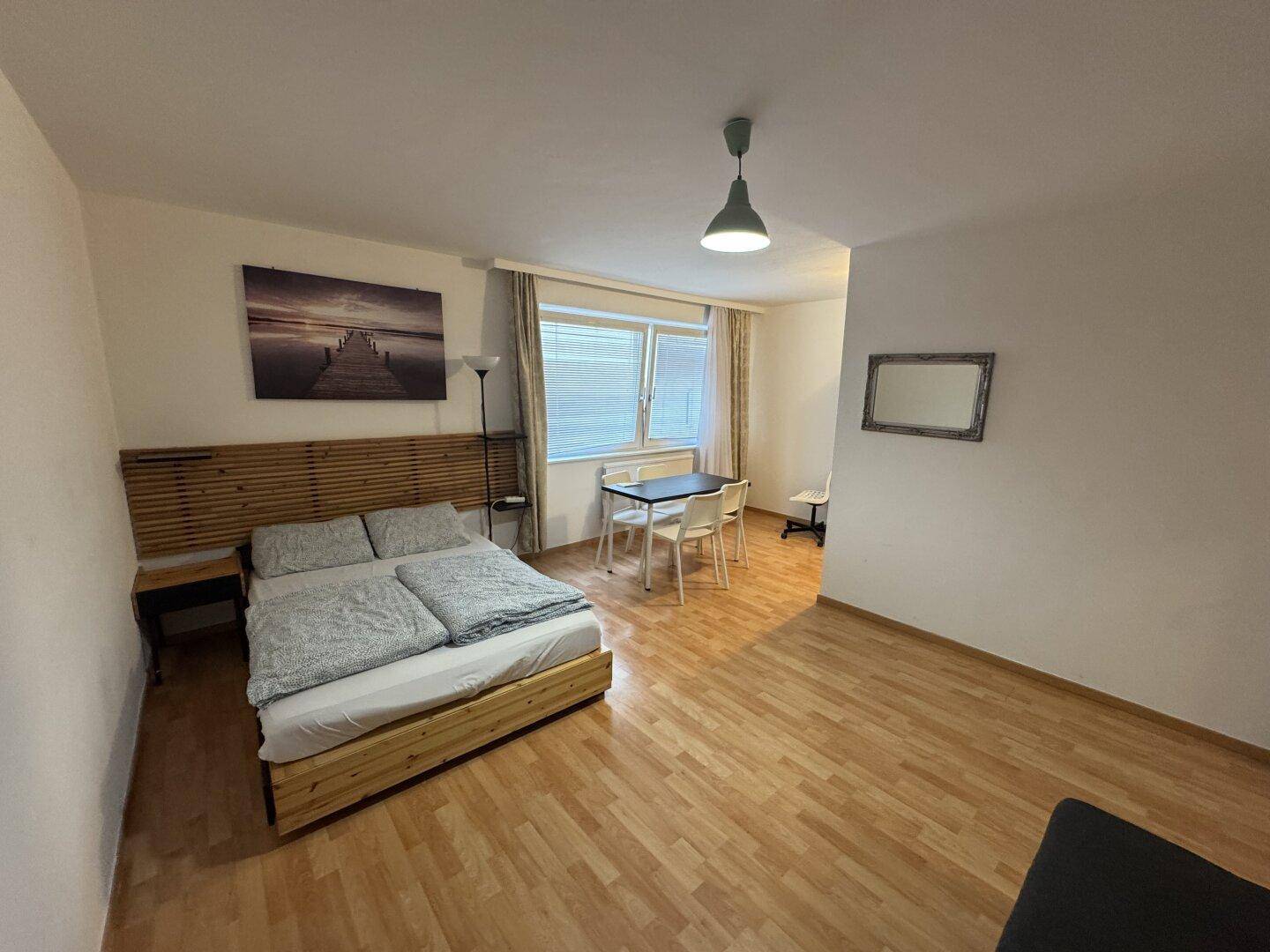 Geräumiges Studio-Apartment mit hellem Laminatboden und funktionaler Einrichtung.