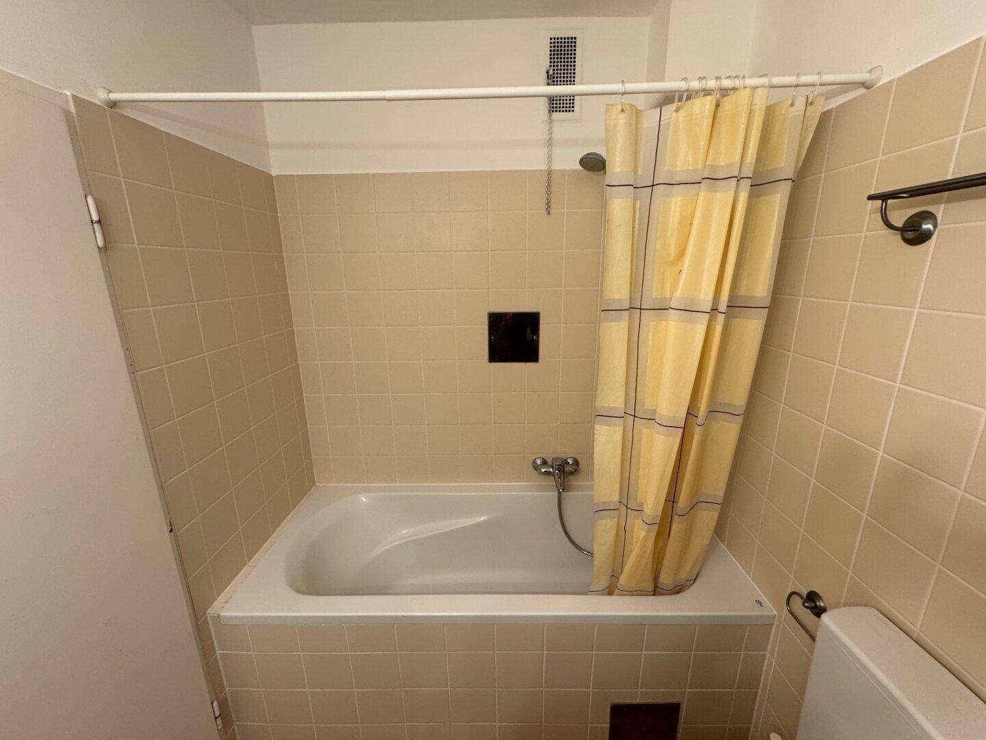 Badezimmer mit Badewanne und Duschvorhang, gefliest in neutralen Beigetönen.