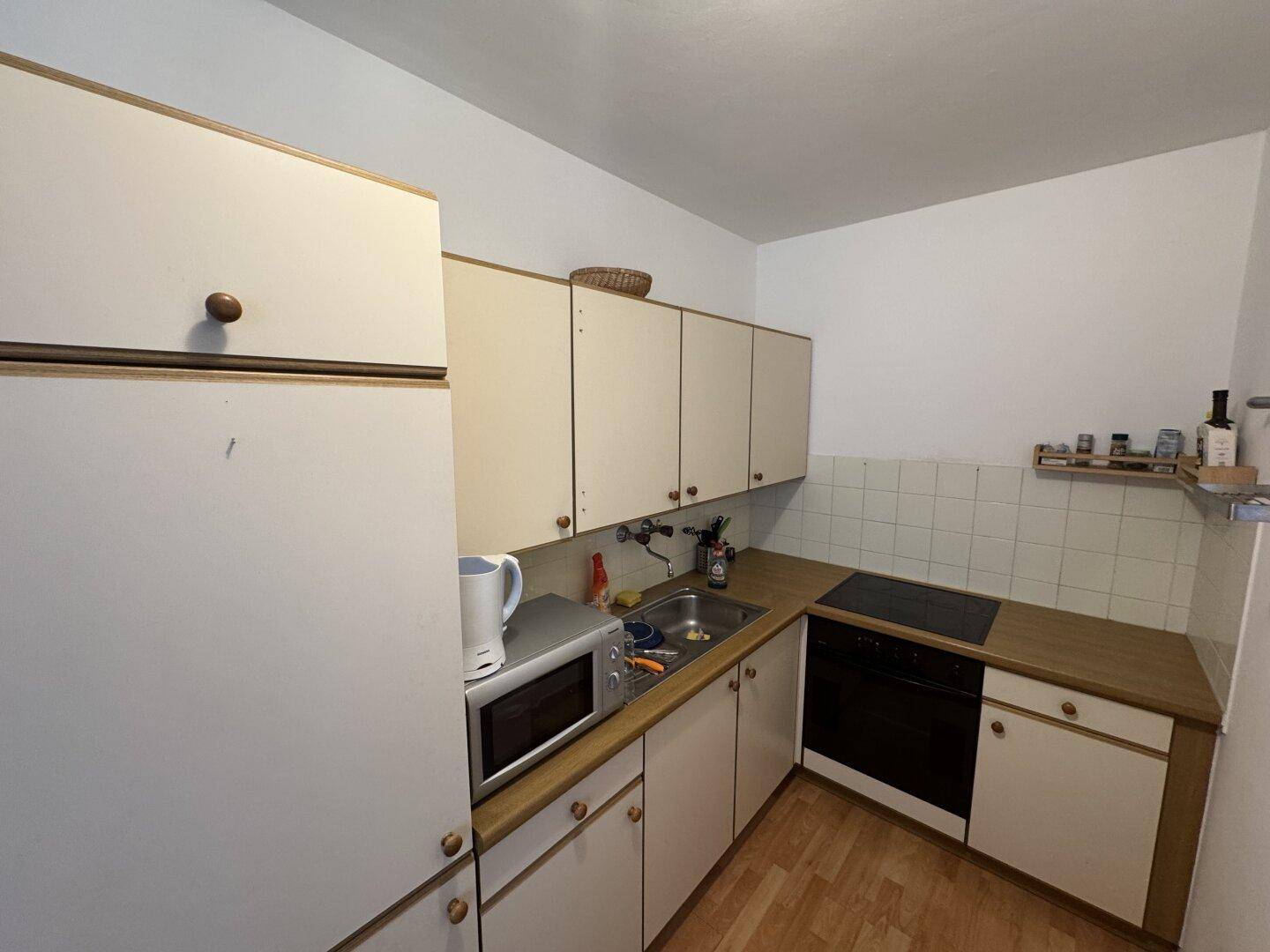 Funktionale Küche mit weißen Schränken, Holz-Arbeitsplatte und grundlegenden Geräten.