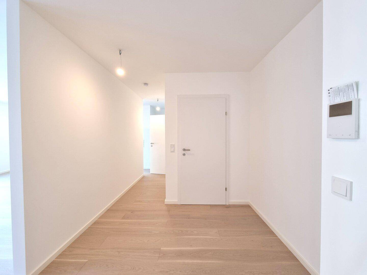 Heller Flur mit Holzboden und weißen Wänden, der zu weiteren Räumen in der Wohnung führt.