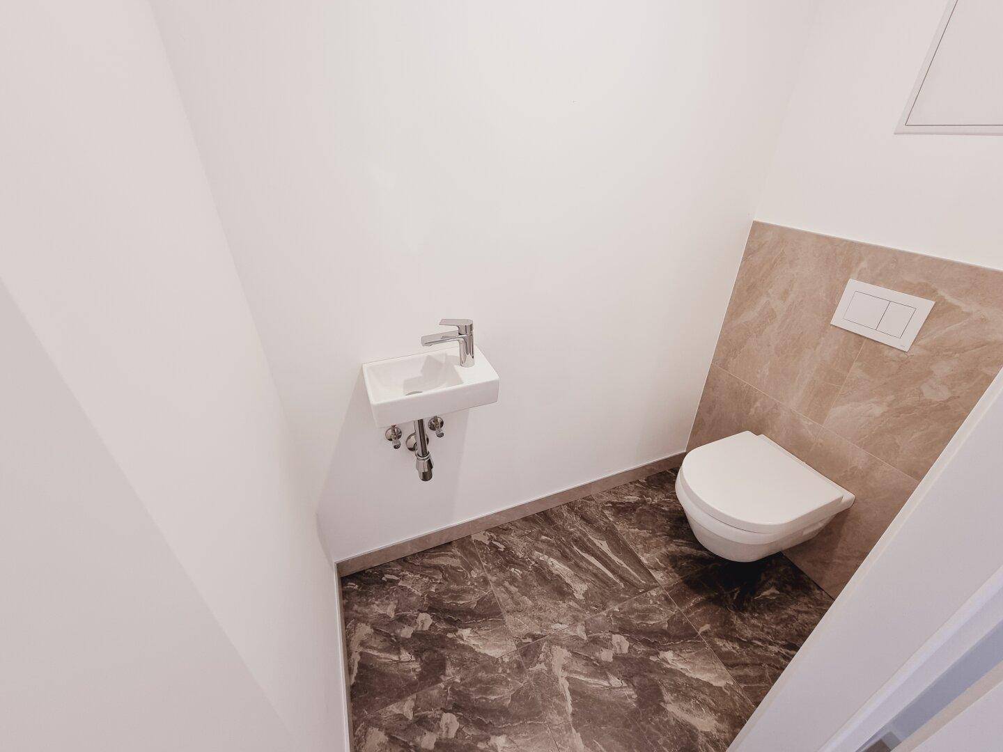 Modernes Gäste-WC mit Wand-WC, kleinem Waschbecken und dunklen Fliesen an Boden und Wand.