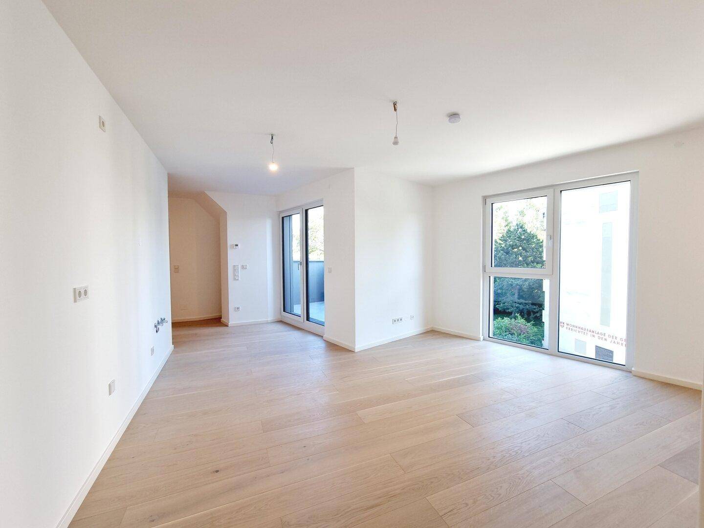 Geräumiges, helles Zimmer mit Holzboden und großen Fenstern, die einen Blick ins Grüne bieten.