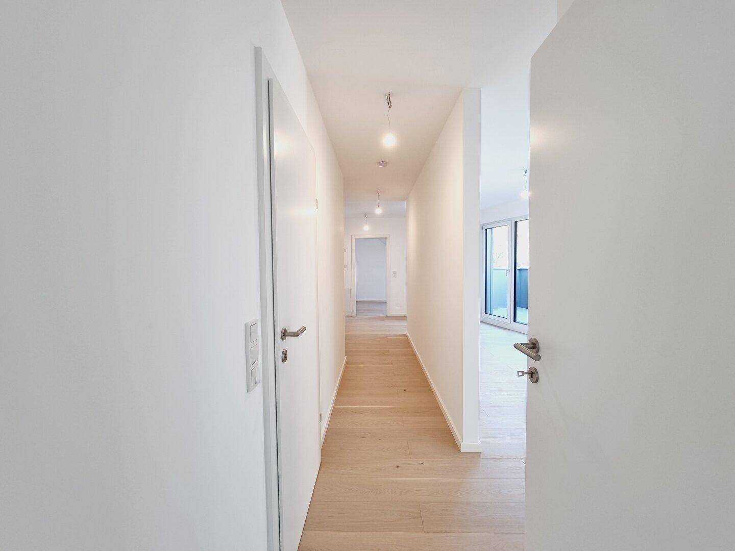 Heller Flur mit Holzboden und weißen Türen, der zu verschiedenen Räumen der Wohnung führt.