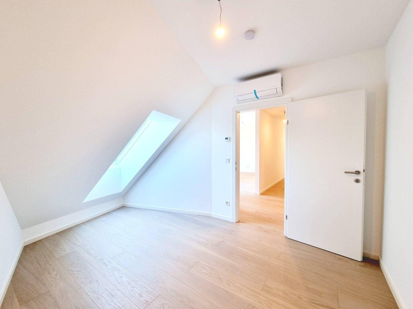Helles Schlafzimmer im Dachgeschoss mit Holzboden, Dachschräge und Klimaanlage.