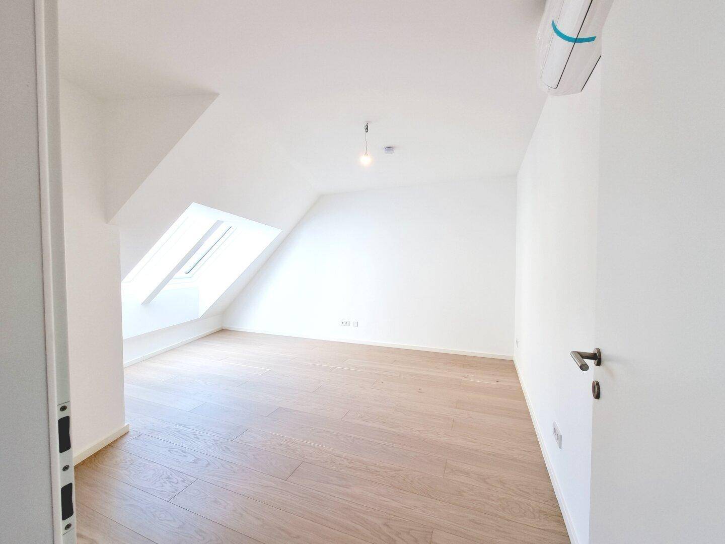 Geräumiges Dachgeschosszimmer mit Holzboden, Dachfenster und weiß gestrichenen Wänden.
