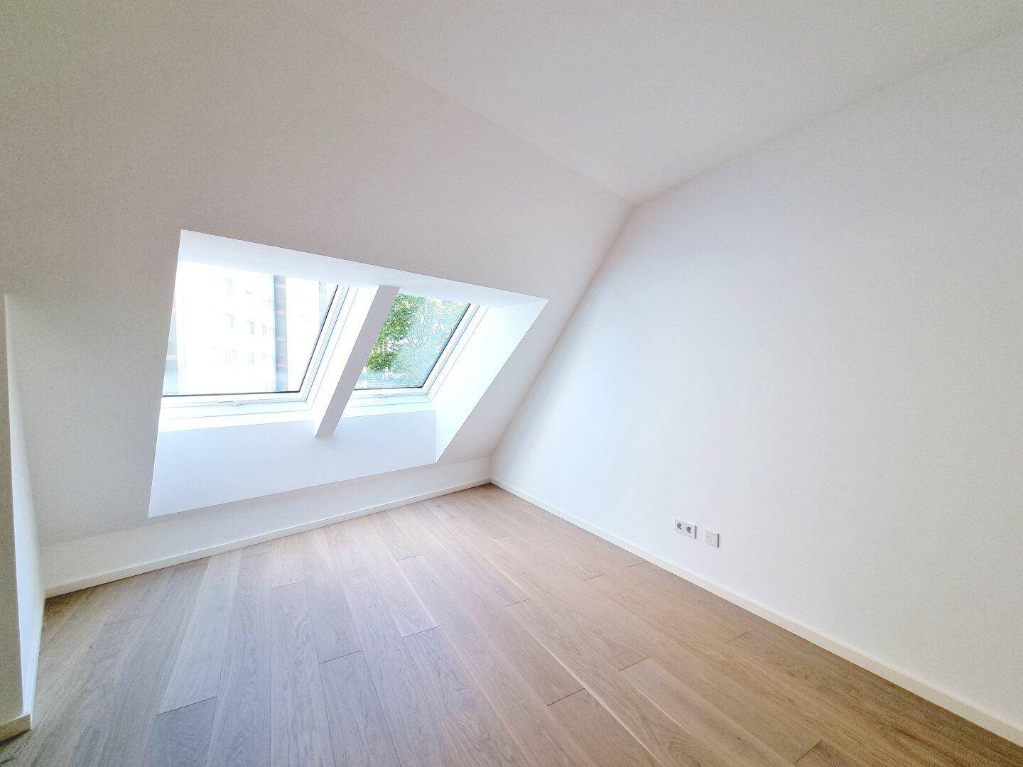 Dachgeschosszimmer mit Holzboden und großem Dachfenster, das einen Blick nach draußen bietet.