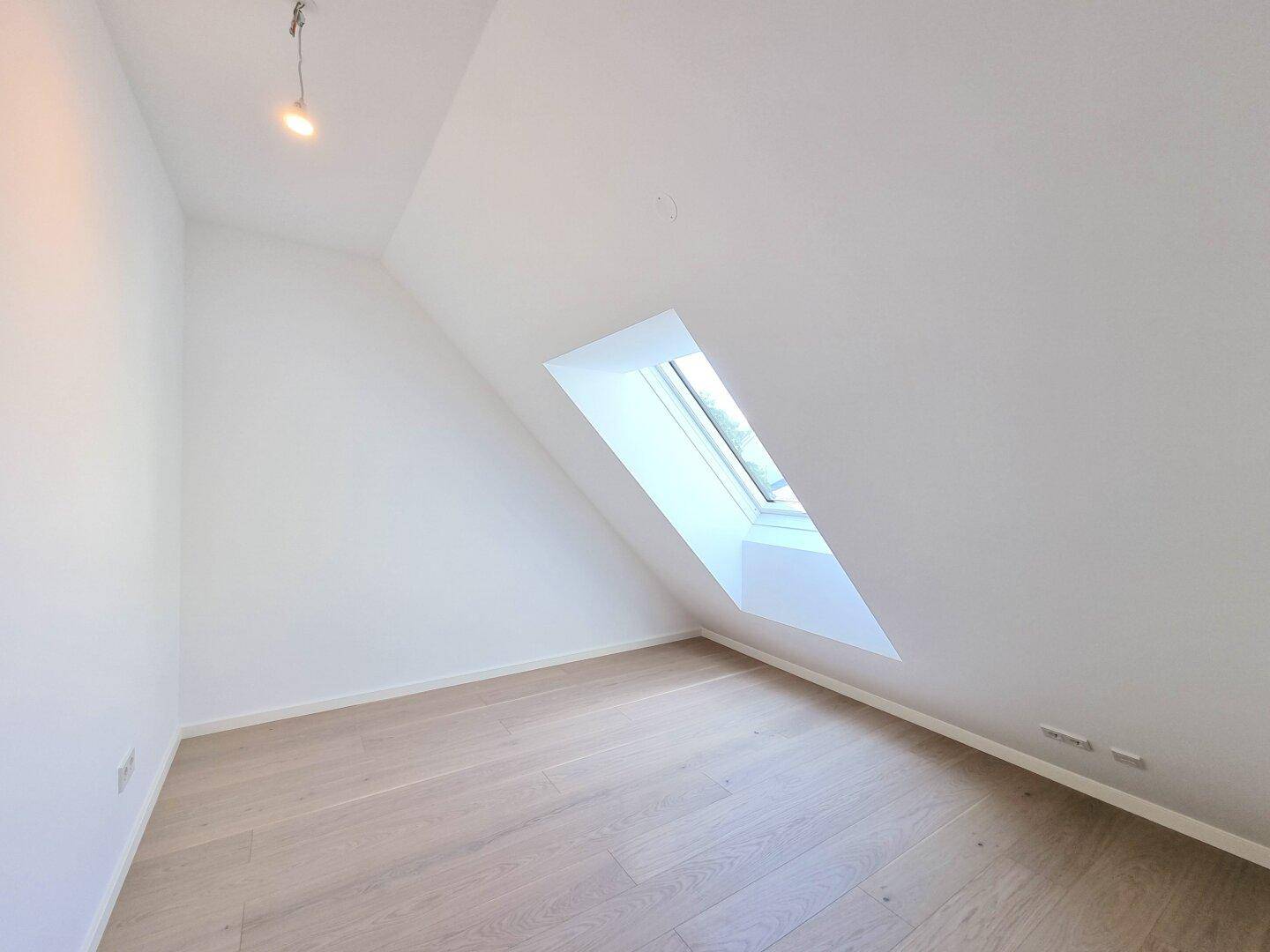 Ruhiges Dachgeschosszimmer mit Holzboden und schrägem Dachfenster, ideal als Schlaf- oder Arbeitszimmer.