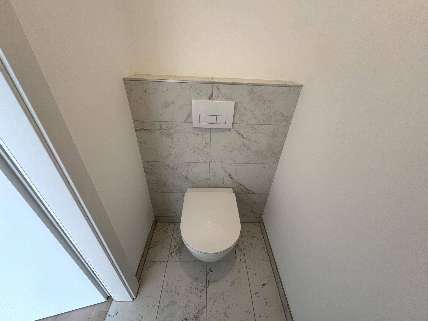 Modernes Wand-WC mit Spülkasten in der Wand und hellen Fliesen im Gästebad.