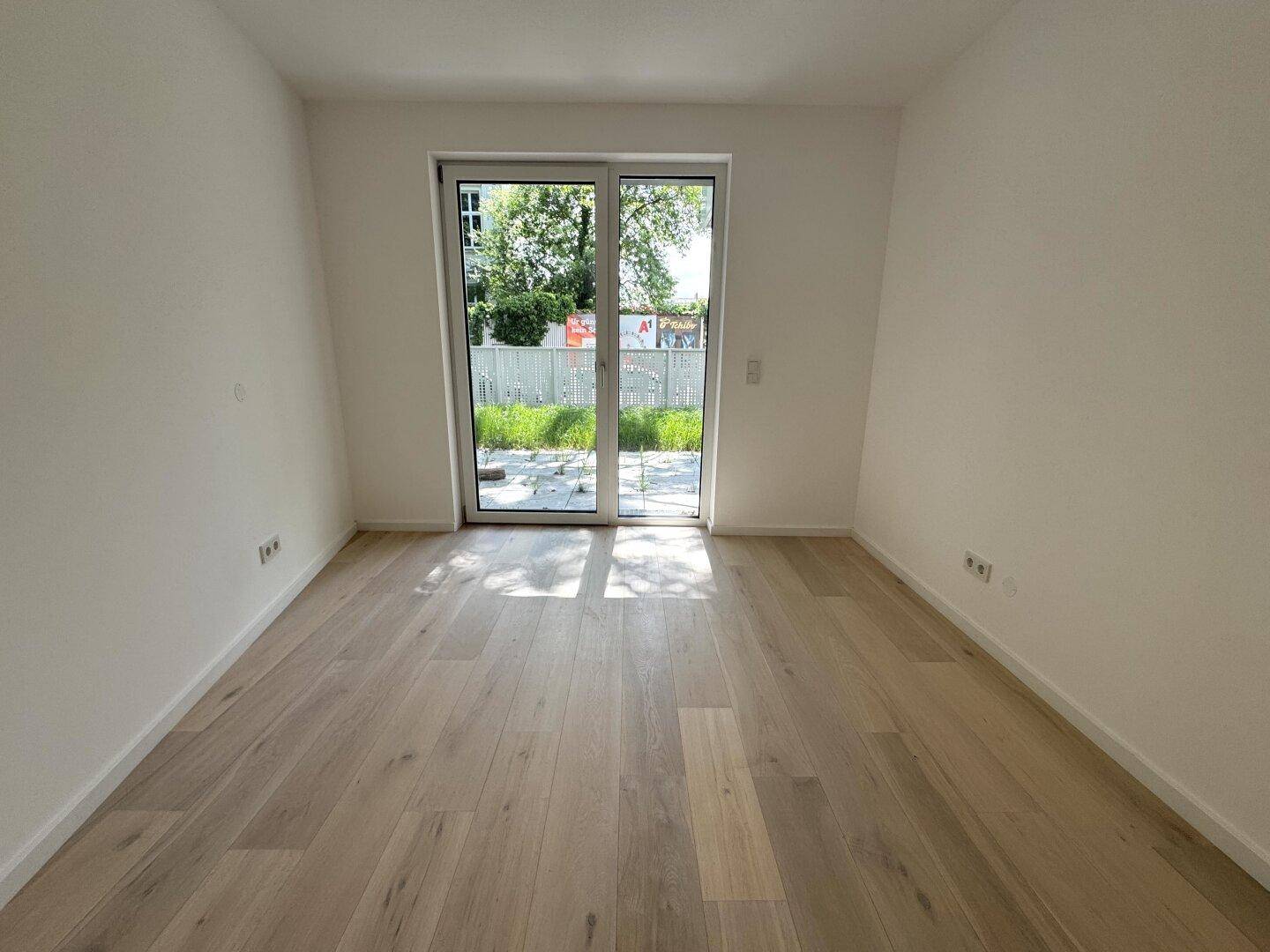 Heller Wohnraum mit hellem Holzfußboden und großer Glastür zum Gartenbereich.