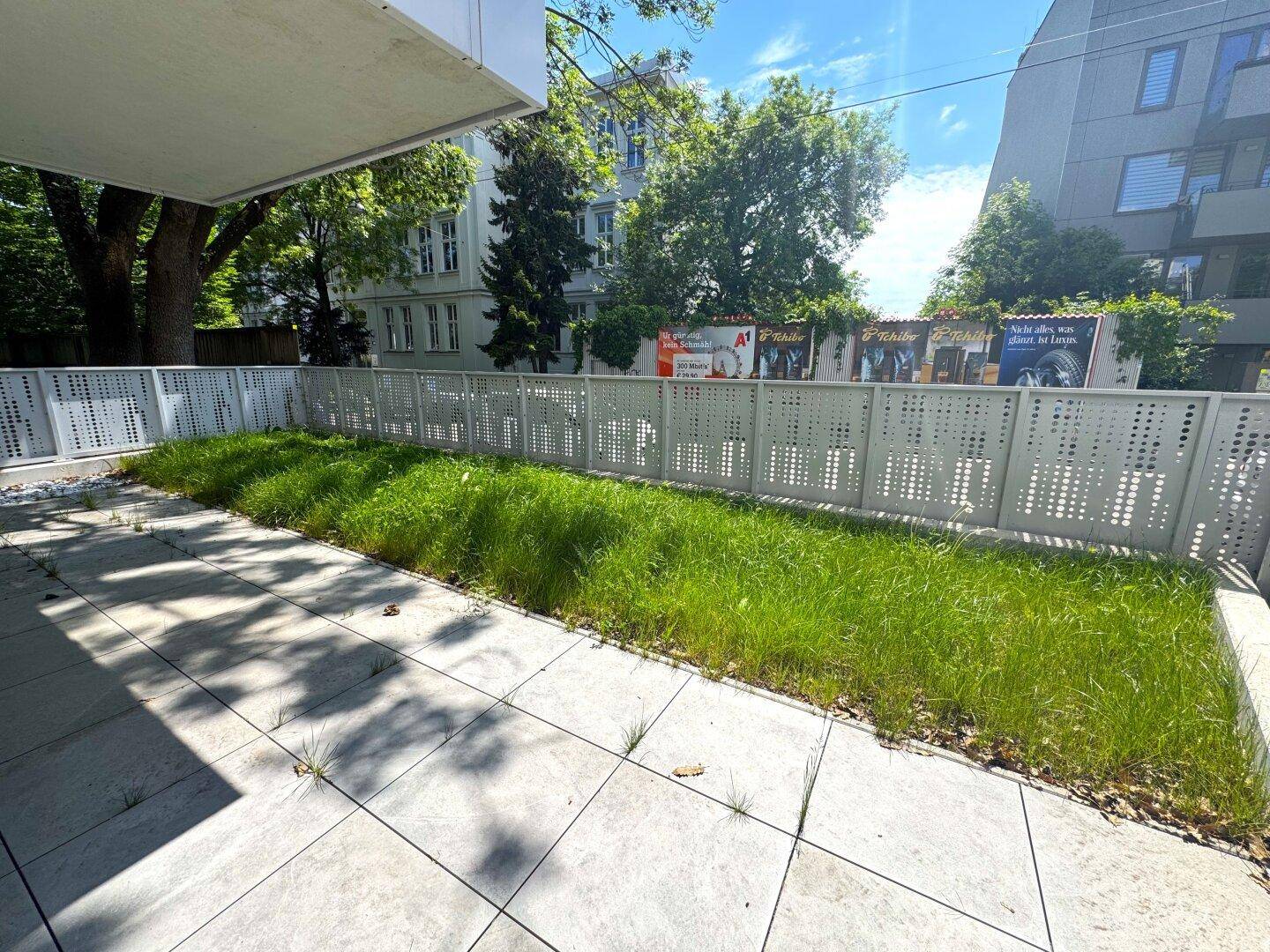 Gepflasterte Terrasse mit Rasenstreifen, umgeben von einem modernen Sichtschutzzaun.