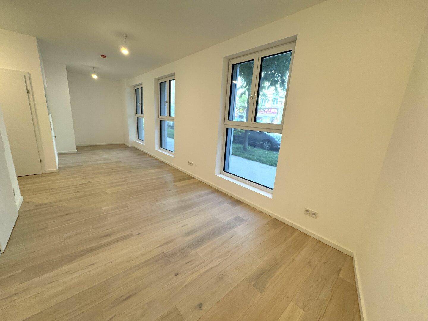 Heller, leerer Raum mit neuem Holzparkettboden und großen Fenstern, die viel Tageslicht hereinlassen.