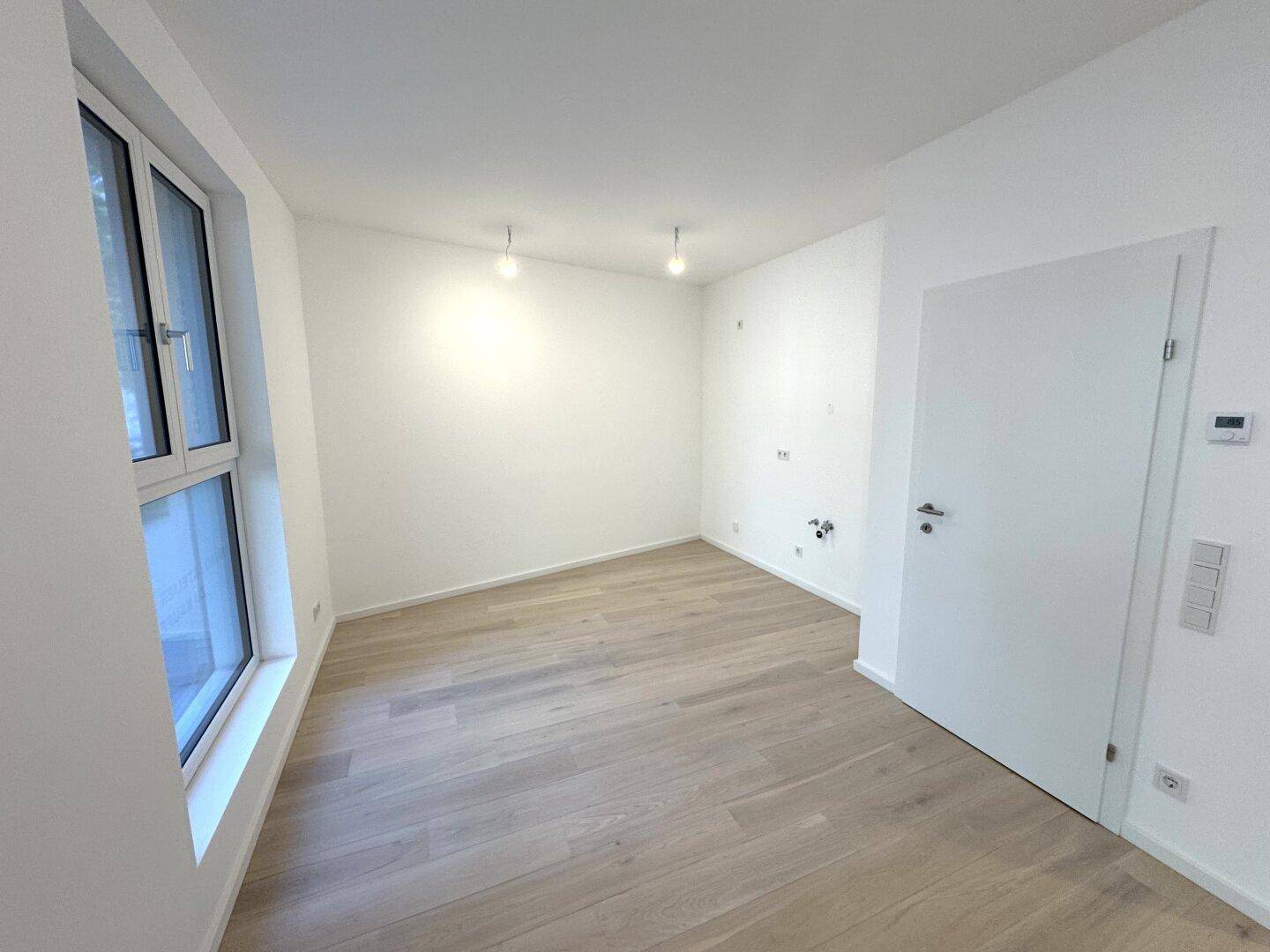 Unmöblierter Raum mit hellem Parkettboden, weißen Wänden und einem Fenster, das für Tageslicht sorgt.