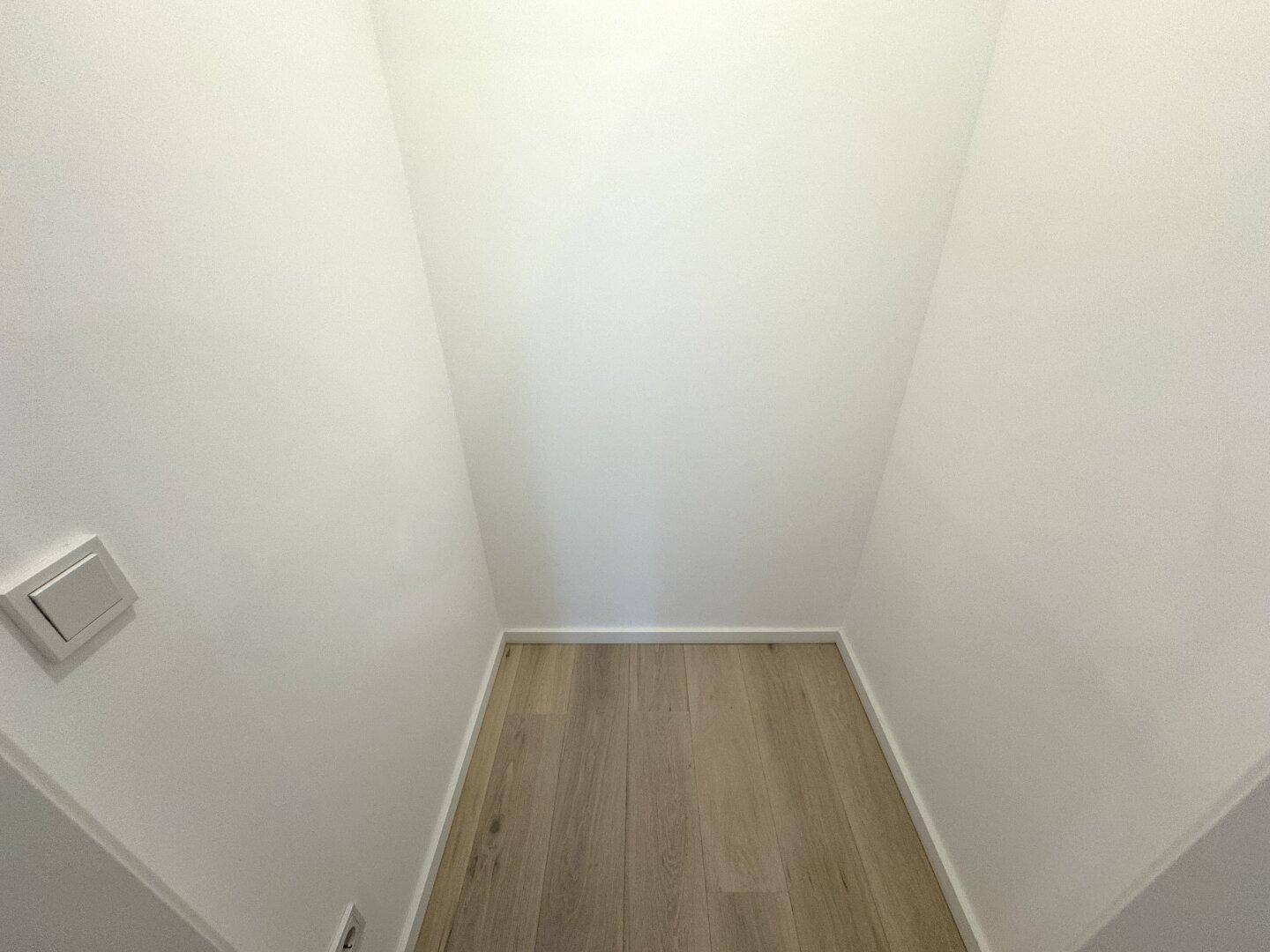 Kleiner, leerer Abstellraum mit hellem Holzboden und weißen Wänden, ideal für zusätzlichen Stauraum.