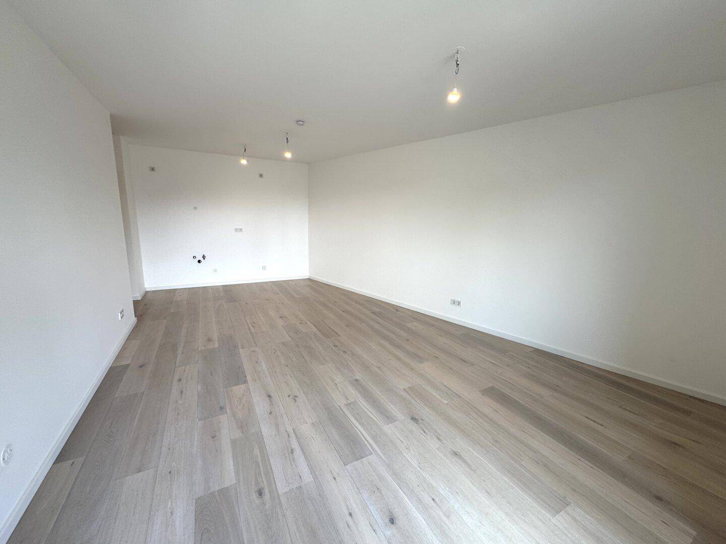 Geräumiges, unmöbliertes Zimmer mit hellem Holzboden und weißen Wänden.