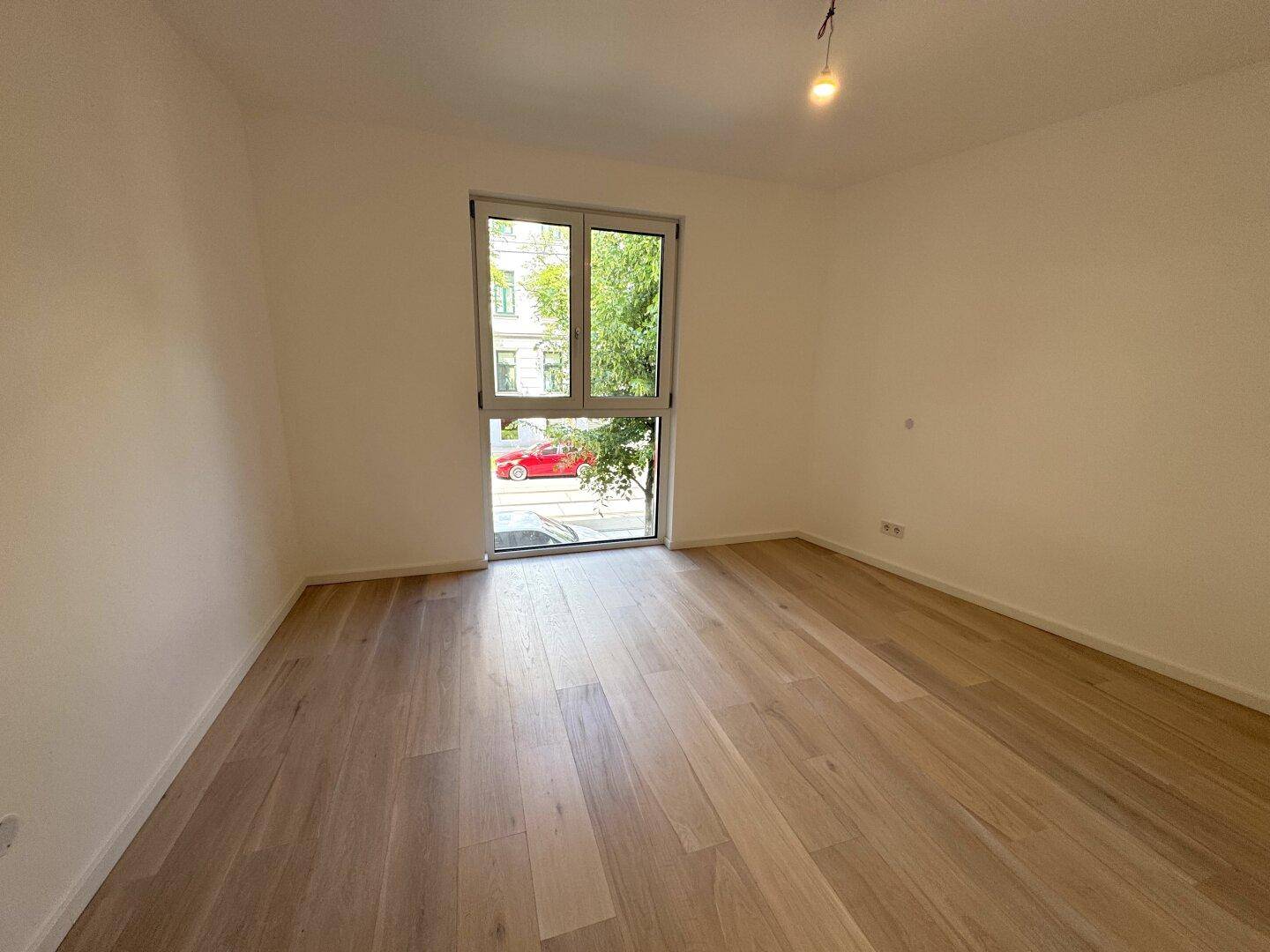 Helles Zimmer mit Holzboden und großem Fenster zur Straße, ideal als Schlafzimmer.
