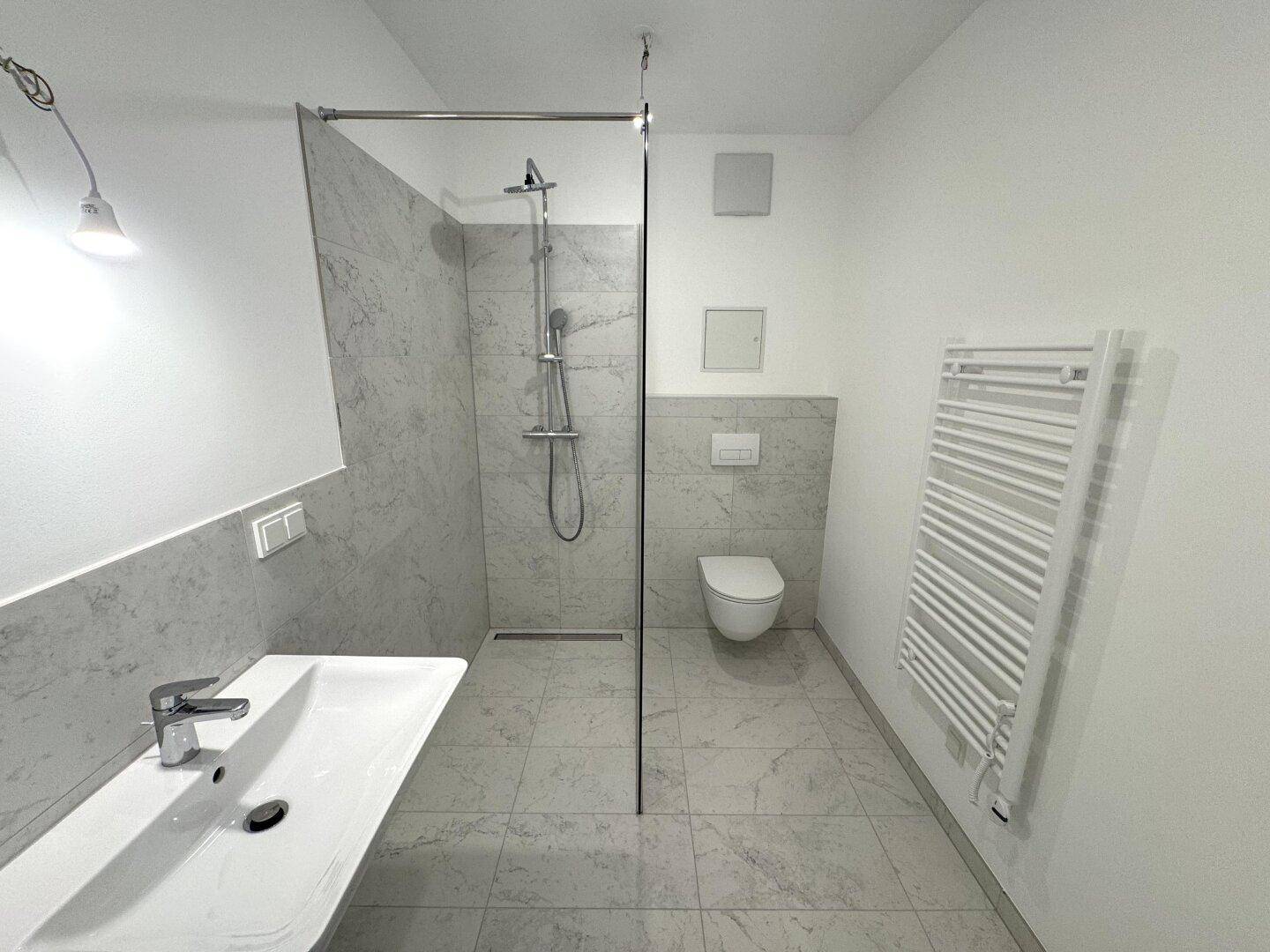 Modernes Badezimmer mit ebenerdiger Dusche, Wand-WC und beheiztem Handtuchhalter.