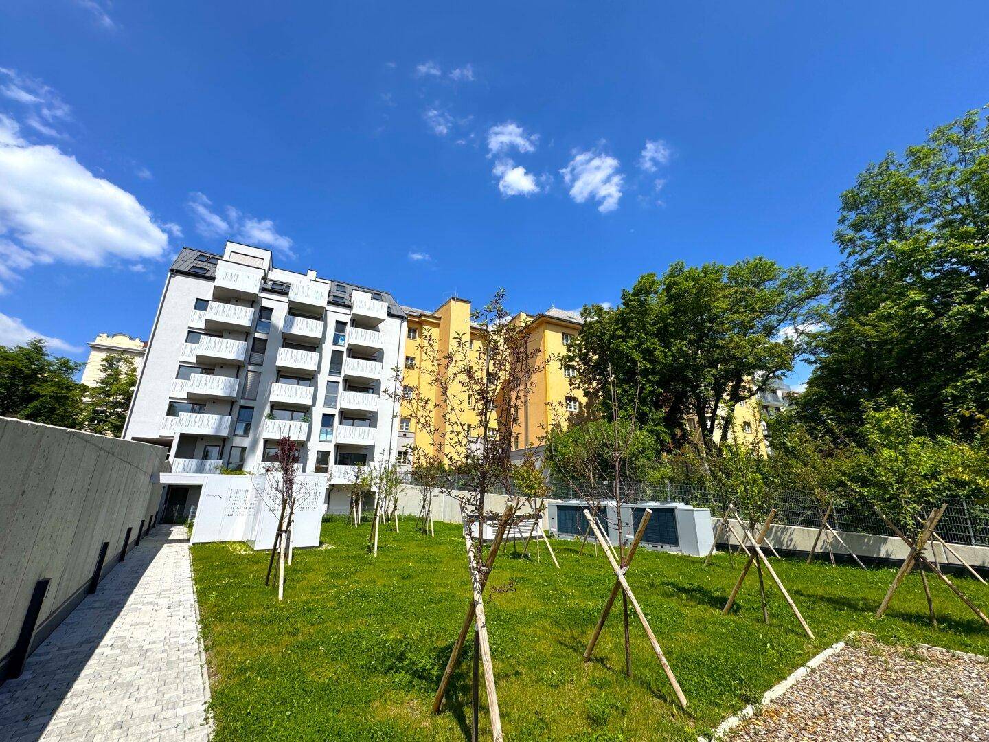 Neubau-Apartmentkomplex mit zeitgenössischer Architektur und gepflegten Grünflächen unter blauem Himmel.