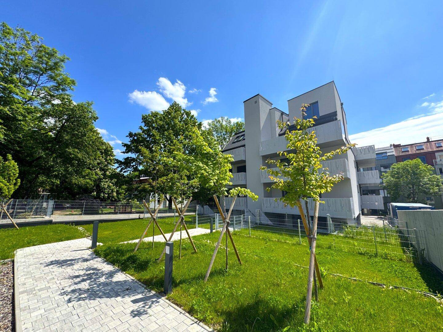 Seitenansicht des modernen Apartmentgebäudes mit grüner Rasenfläche und jungen Bäumen unter klarem Himmel.