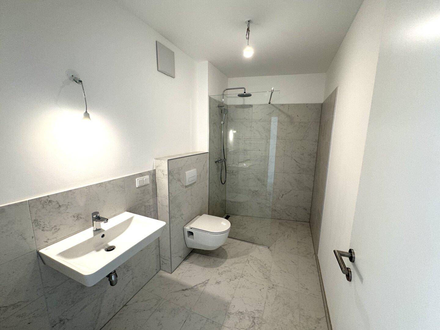 Modernes Badezimmer mit großformatigen Fliesen, wandhängendem WC und ebenerdiger Dusche.