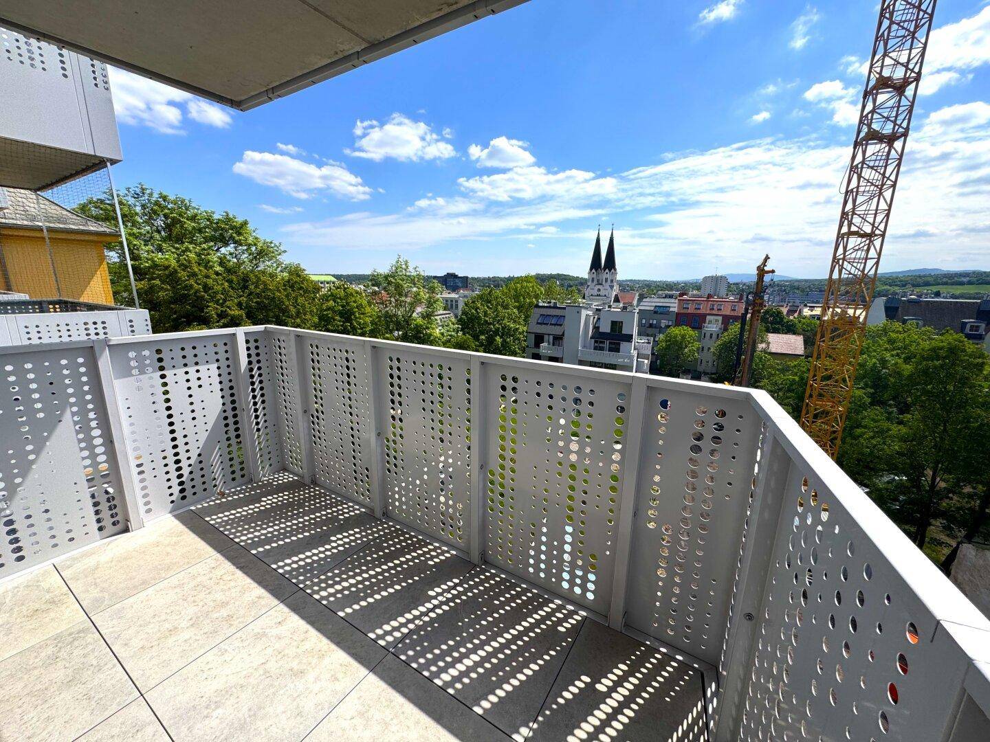 Heller Balkon mit modernem Lochblechgeländer und Blick auf die Stadt und den Kirchturm.