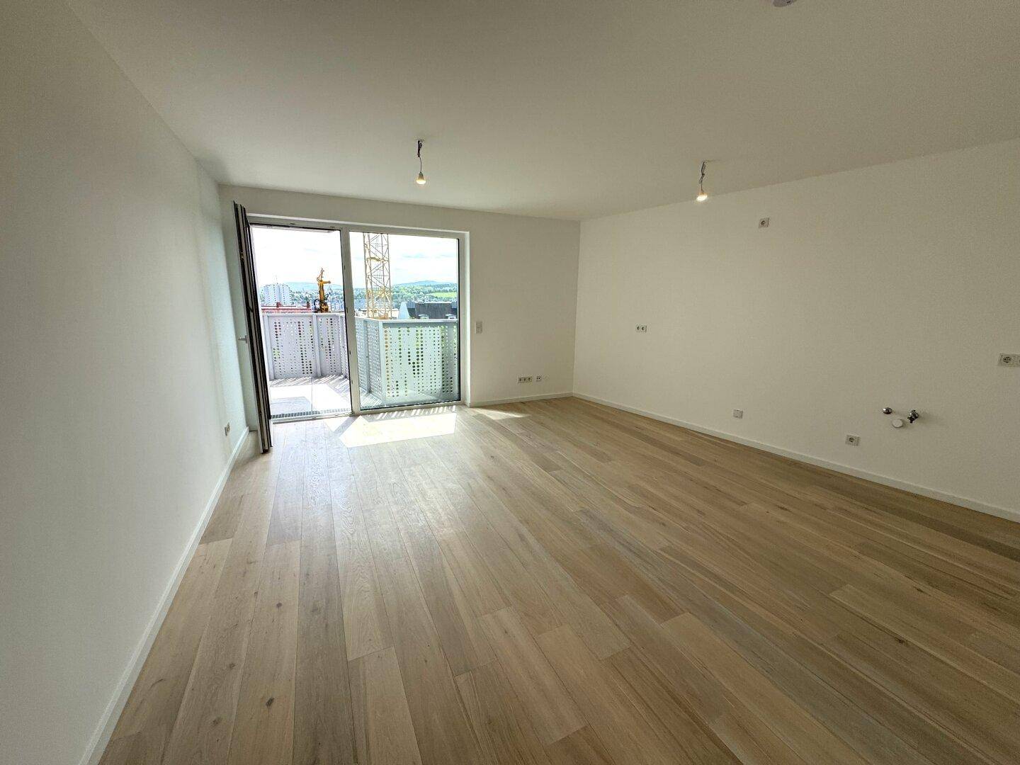 Heller Wohnbereich mit Holzboden und Zugang zu einem Balkon mit Weitblick.