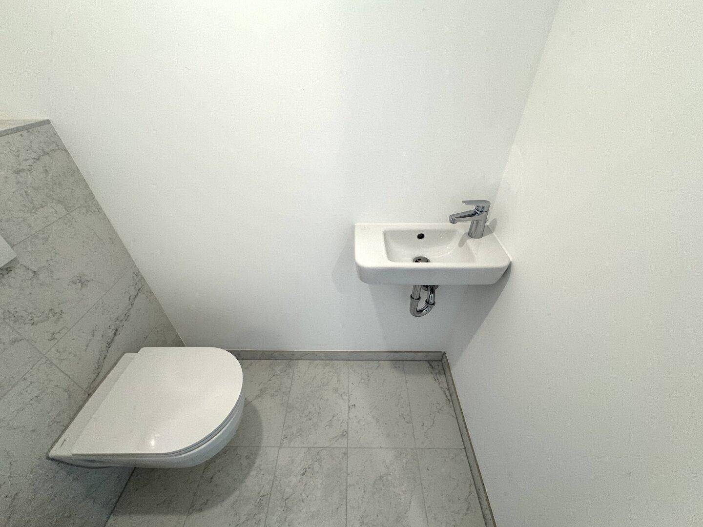 Kompaktes Gäste-WC mit wandhängender Toilette und kleinem Waschbecken.