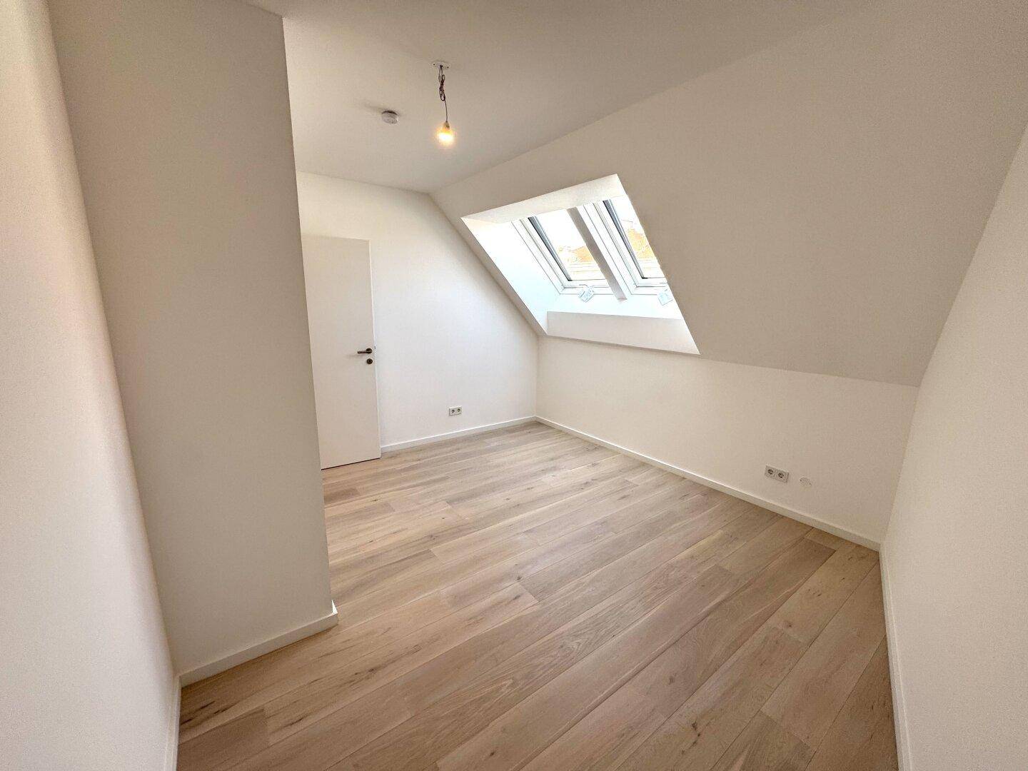 Gemütliches Schlafzimmer mit Holzboden, Dachschräge und mehreren Dachfenstern.