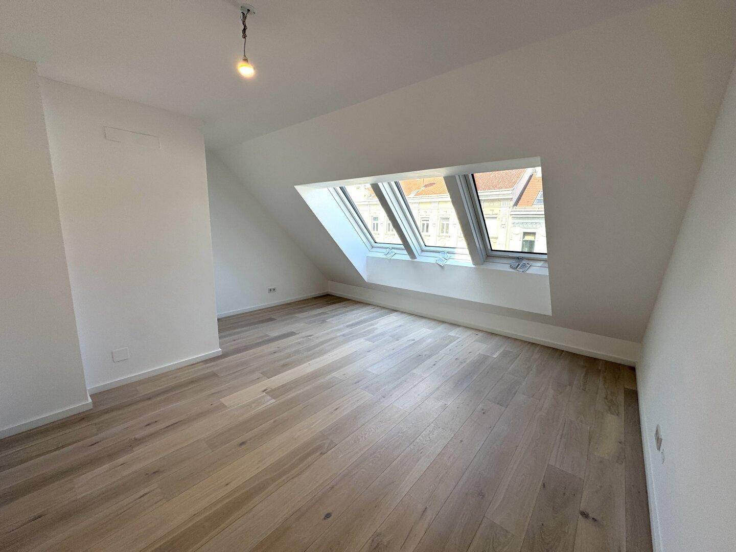 Helles Zimmer mit Holzboden, Dachschräge und großzügigen Dachfenstern.