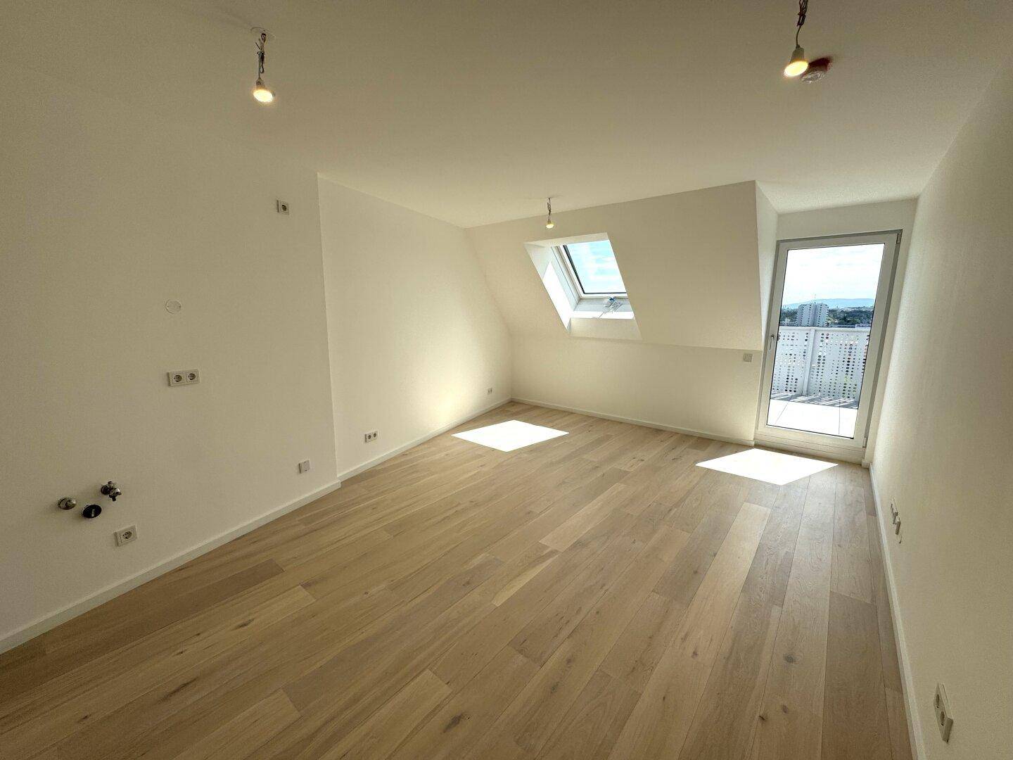 Heller Wohnraum mit Holzboden, Dachschräge und Zugang zu einem Außenbereich.
