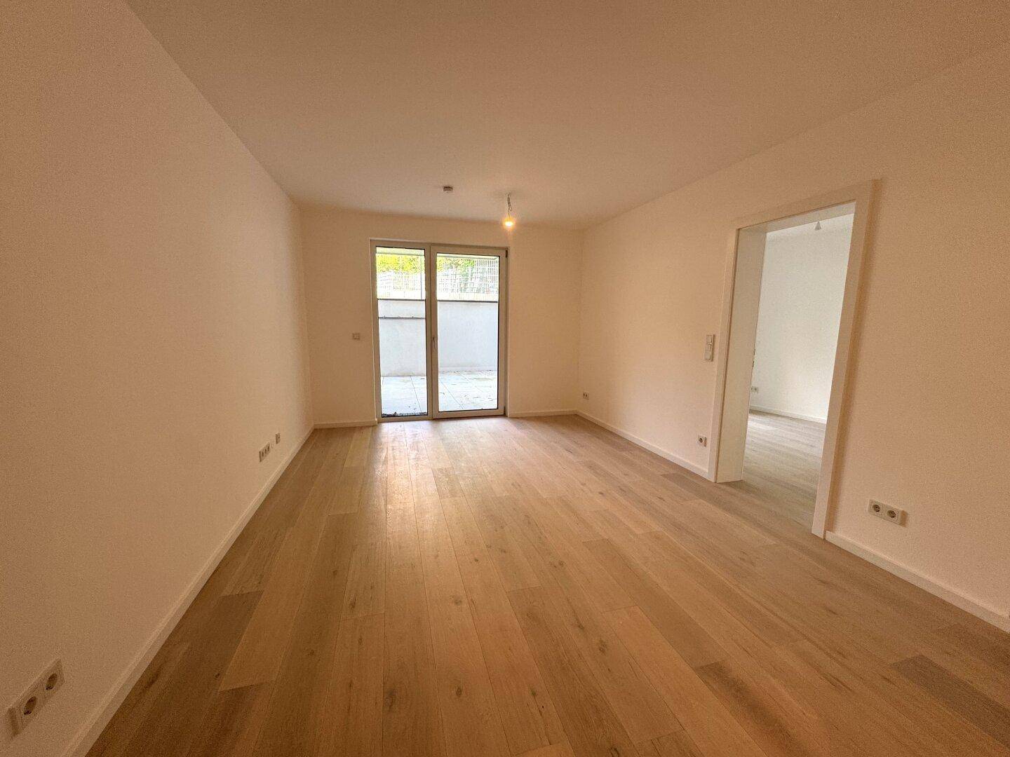 Geräumiges, leeres Zimmer mit hellem Holzfußboden und viel Tageslicht, mit Zugang zu einem weiteren Raum.