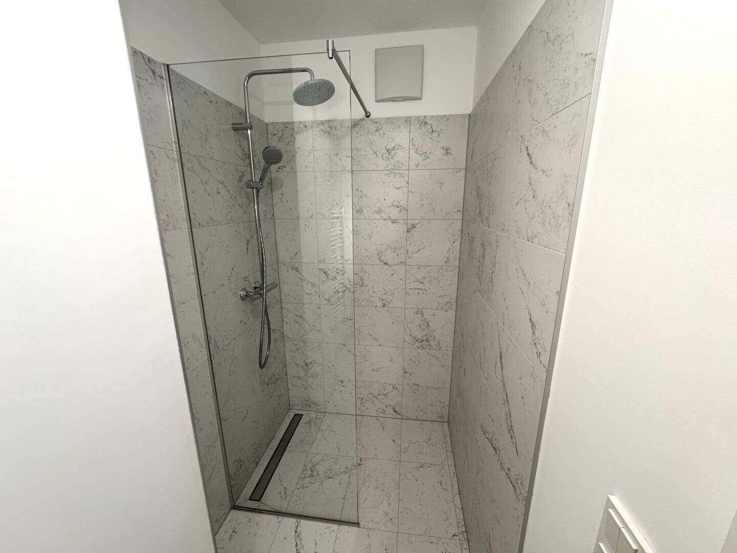 Moderne Duschkabine mit großformatigen Fliesen in Marmoroptik und einer eleganten Regendusche.