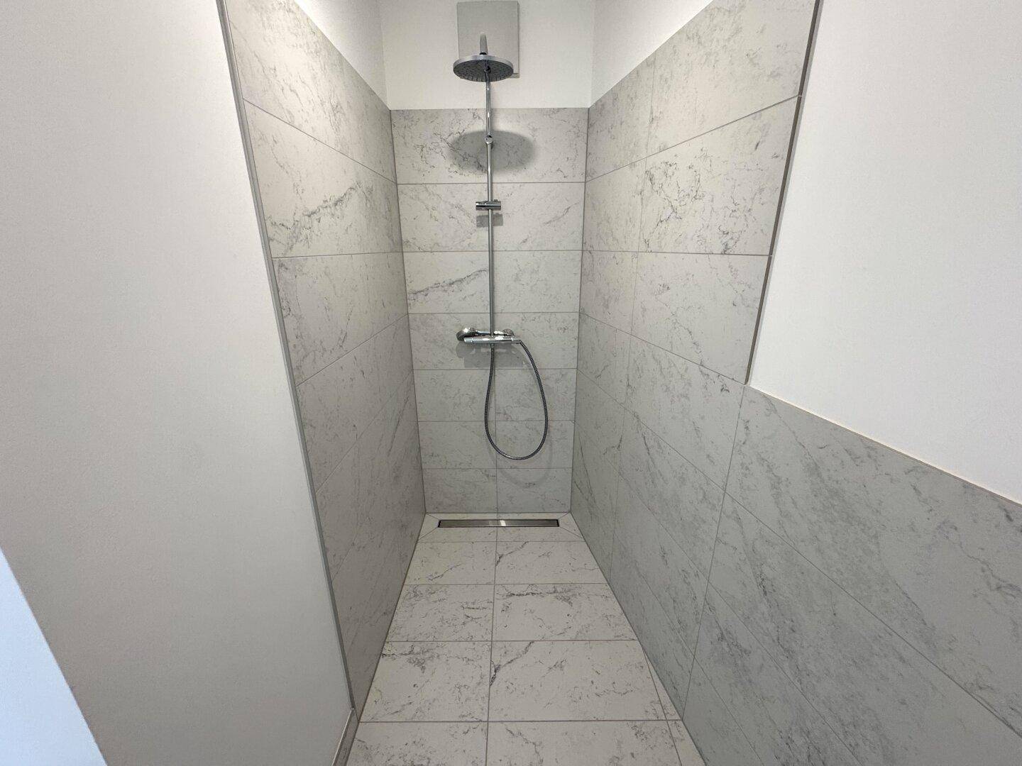 Moderne begehbare Dusche mit großformatigen Fliesen in Marmoroptik und Regendusche.