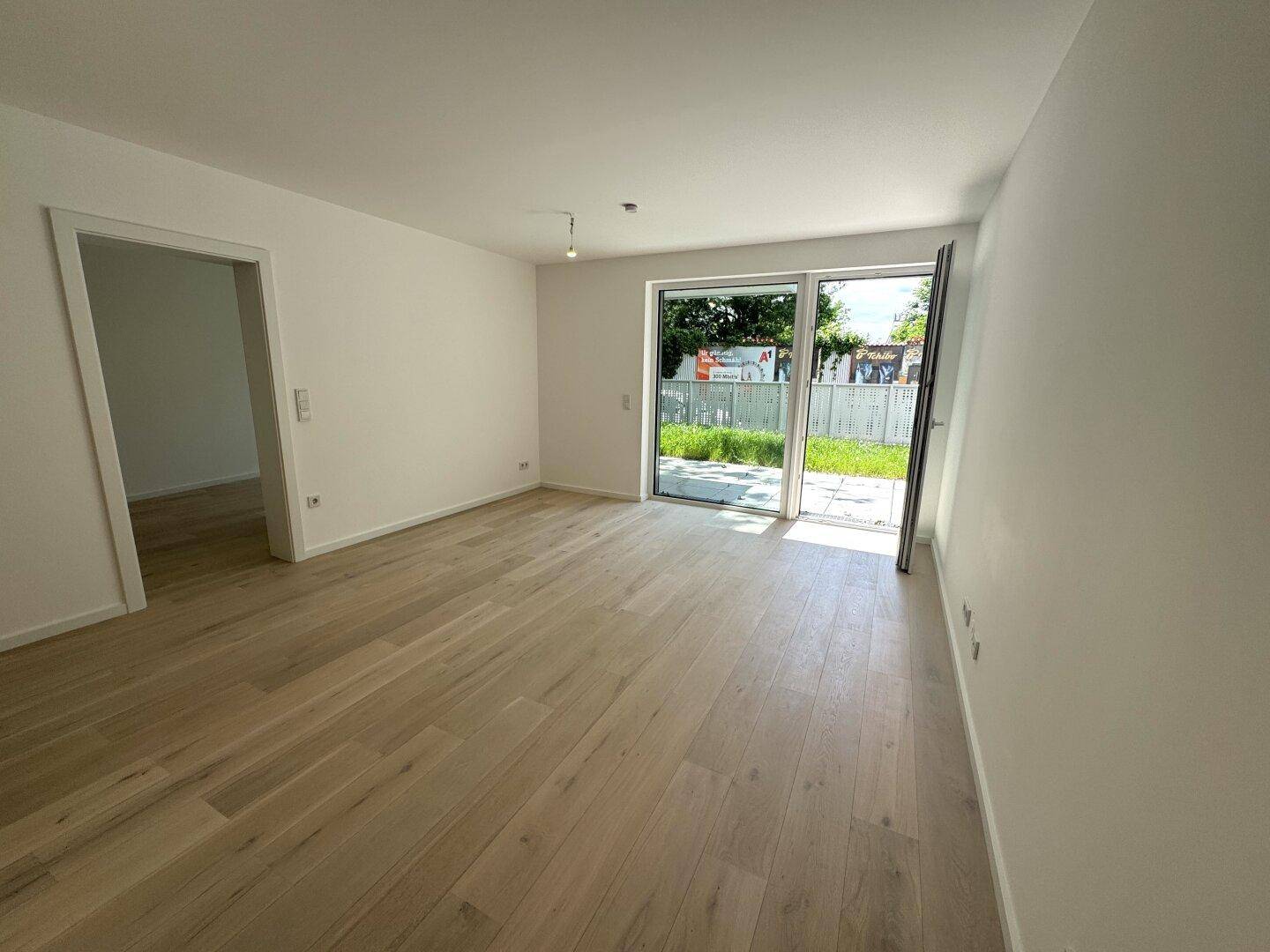 Heller, leerer Raum mit hellem Holzfußboden und Zugang zu einer Außenterrasse.