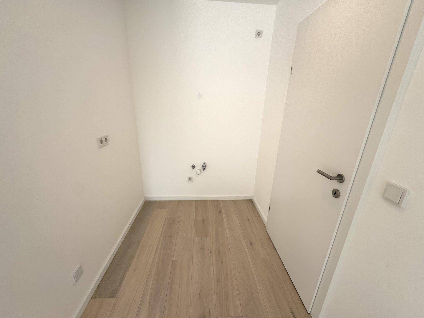 Praktischer Hauswirtschaftsraum mit Holzfußboden und Anschlüssen für Waschmaschine und Trockner.