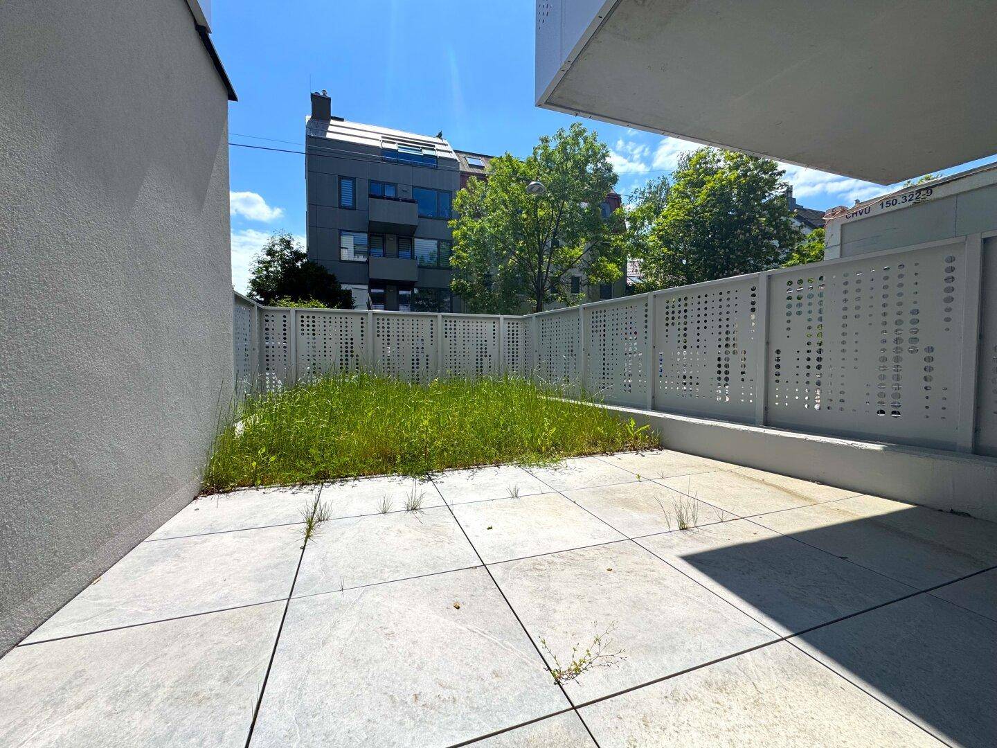 Private Terrasse mit Fliesenboden und kleinem Grünstreifen, umgeben von modernen Sichtschutzelementen.