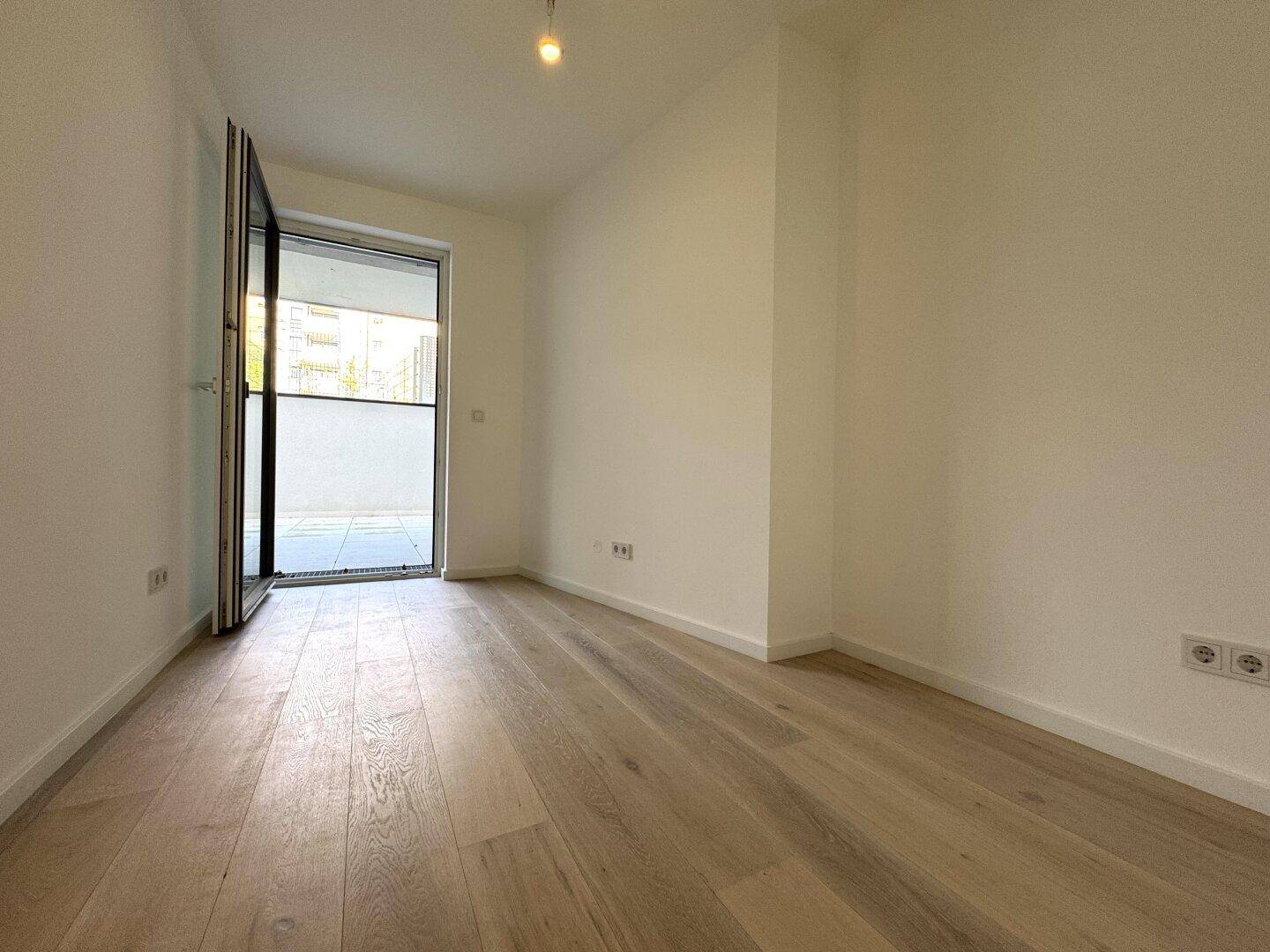 Lichtdurchfluteter Raum mit Holzboden und offener Glastür, die zu einem privaten Außenbereich führt.