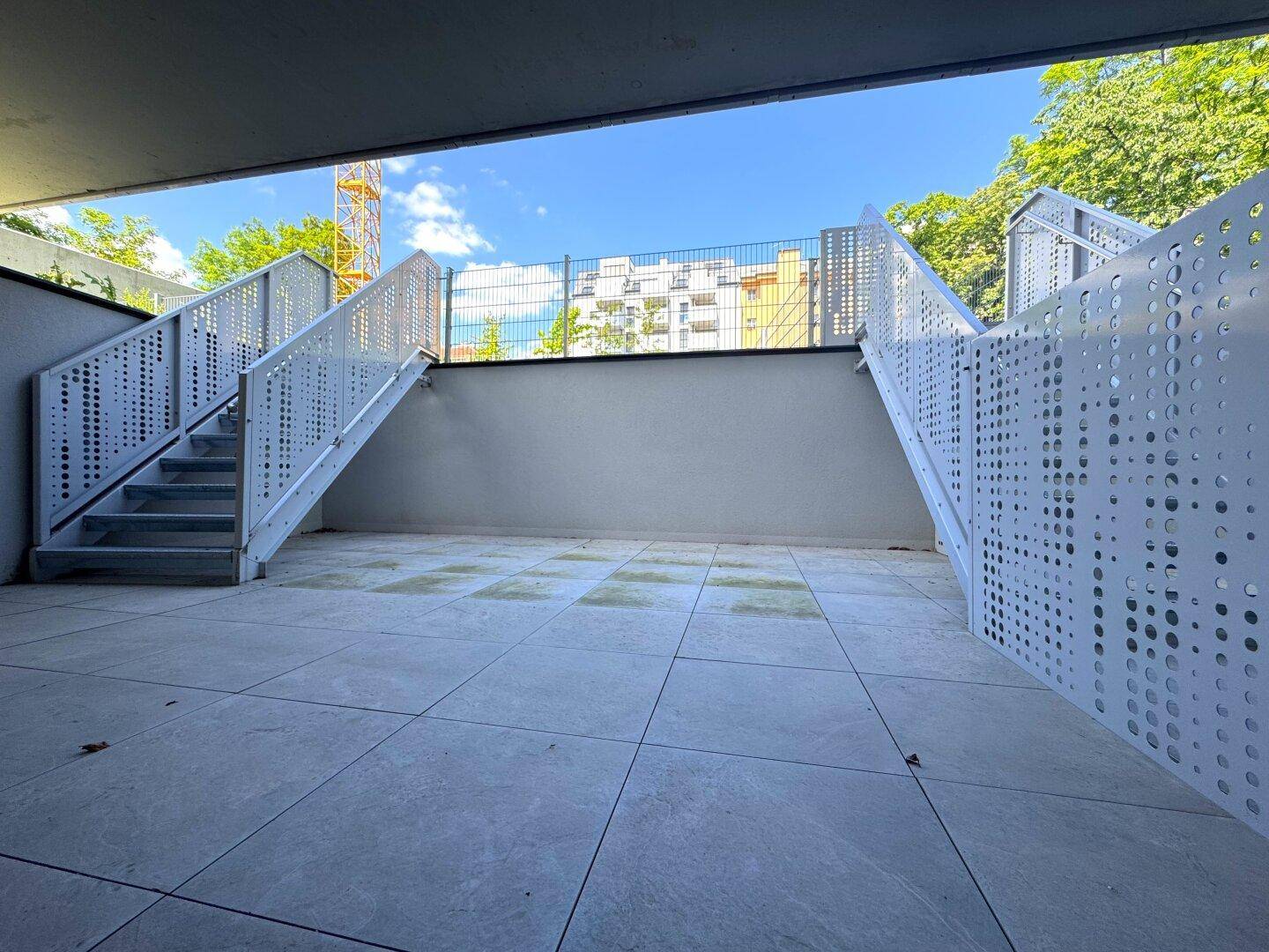 Gedeckter Außenbereich mit modernen Treppen und perforierten Metallgeländern, der zu weiteren Ebenen führt.